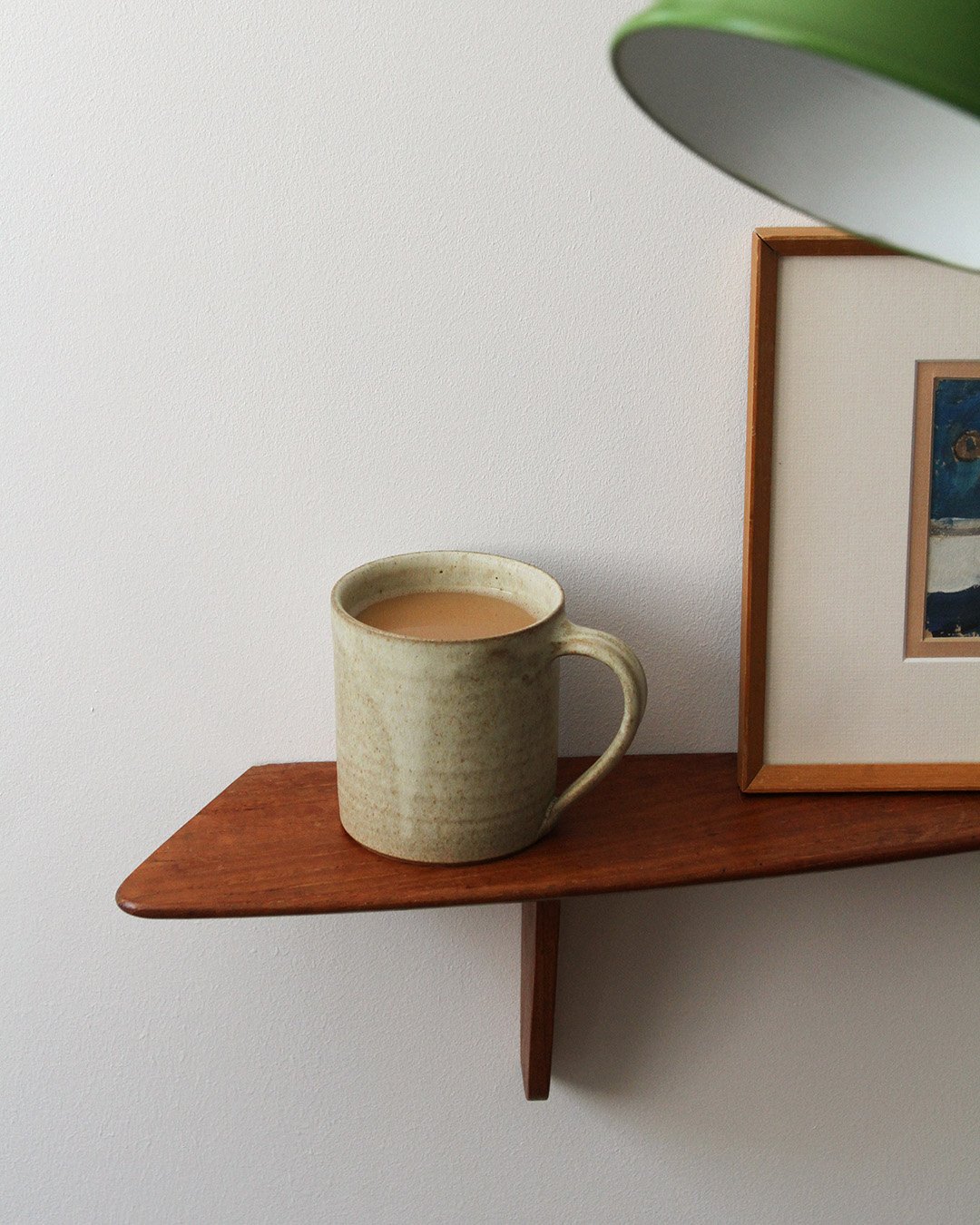 A mug of a tea in a sandy speckled glaze shown on a wooden shelf