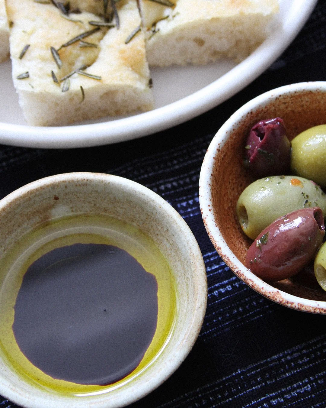 A close up detail of a little bowl filled with oil and vinegar, next to a plate of focaccia.