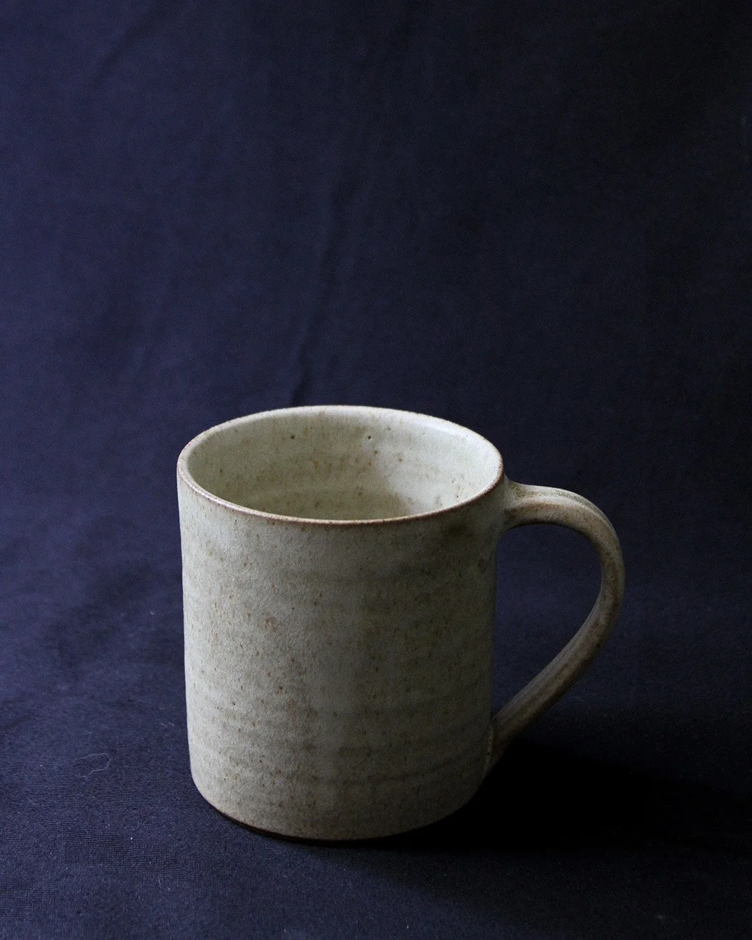 A tea mug in a sandy speckled glaze on a deep blue background