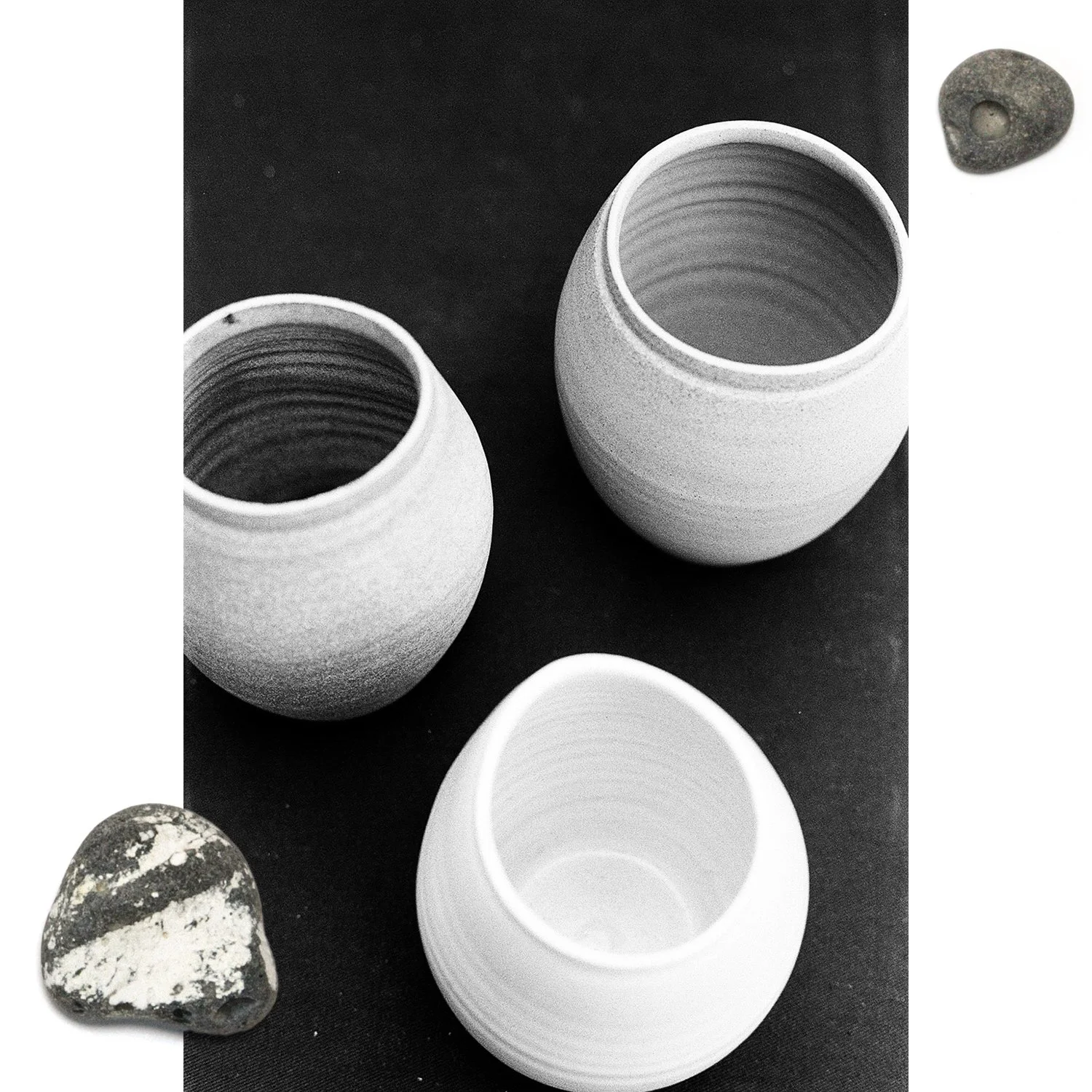 Two ceramic vases with textured surfaces, and two decorative stones, one marble and one dark with white streaks, on a black background.