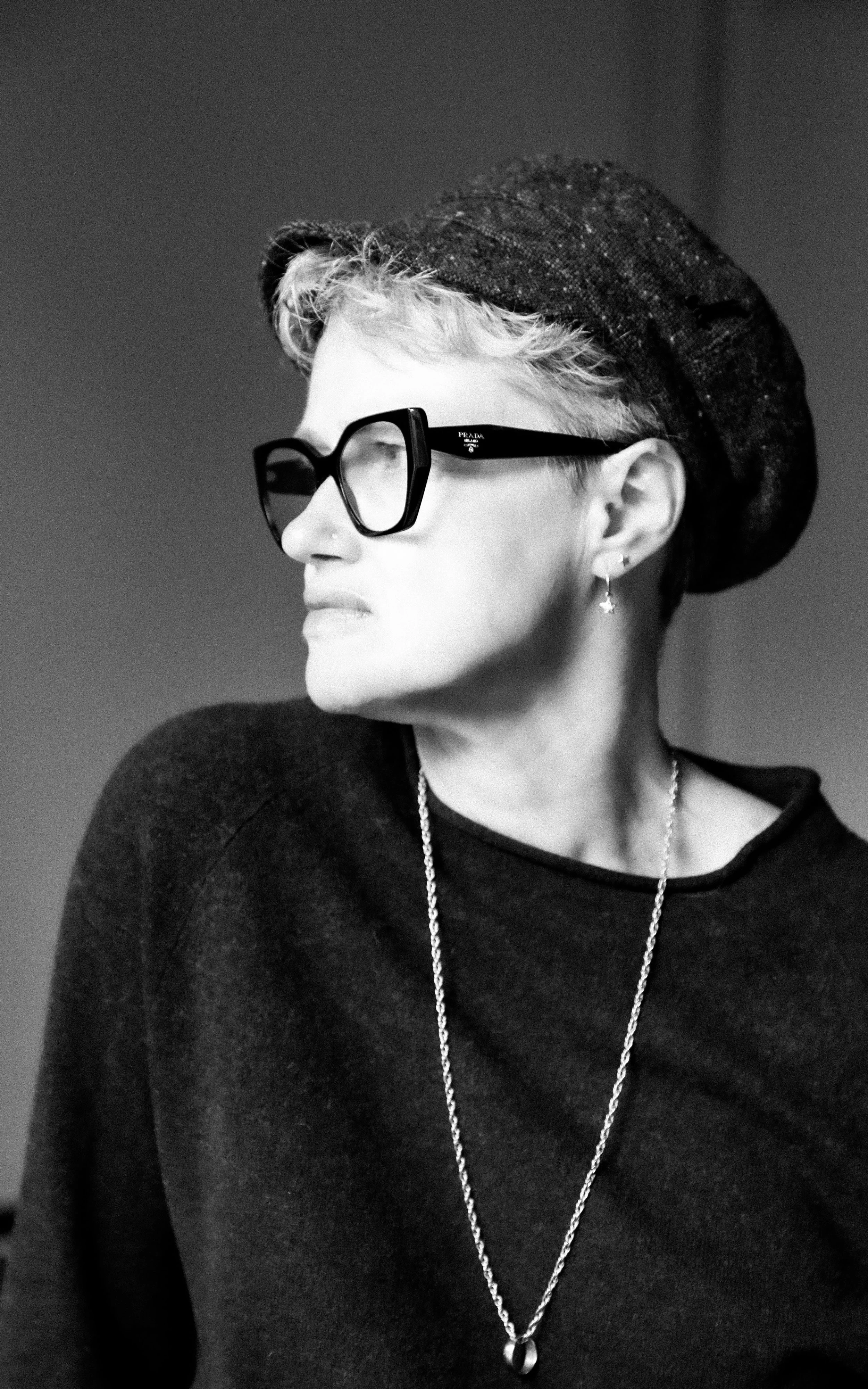 A woman with curly blonde hair, glasses, and lipstick looking at the camera against a plain background.