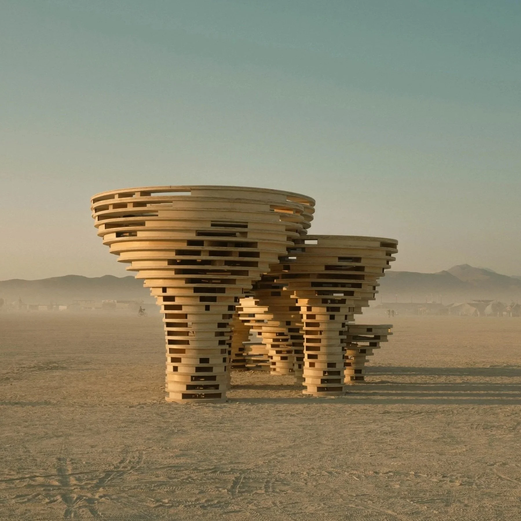 Sculpture of stacked wooden slats resembling elephants in a desert with mountains in the background.