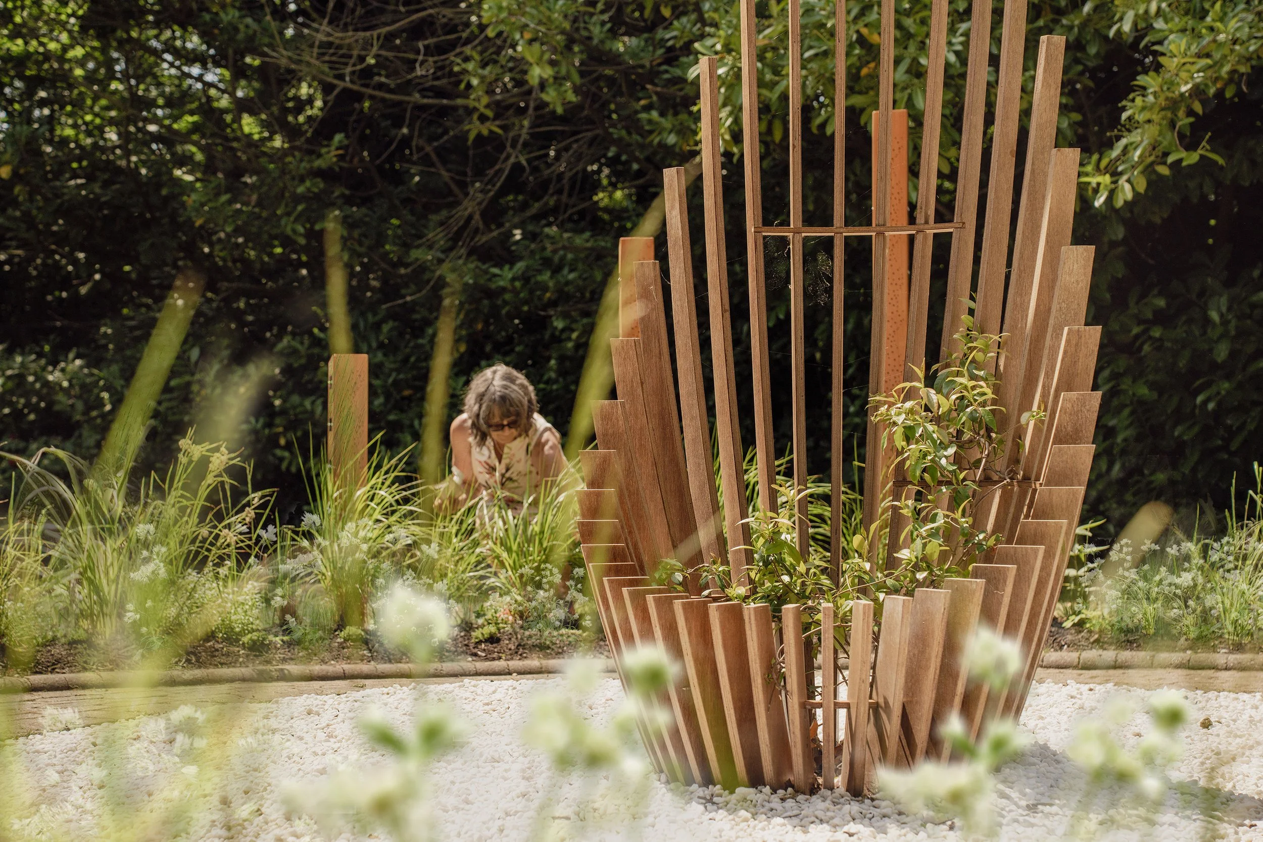 Child exploring a garden with a decorative wooden art installation surrounded by greenery and white gravel.