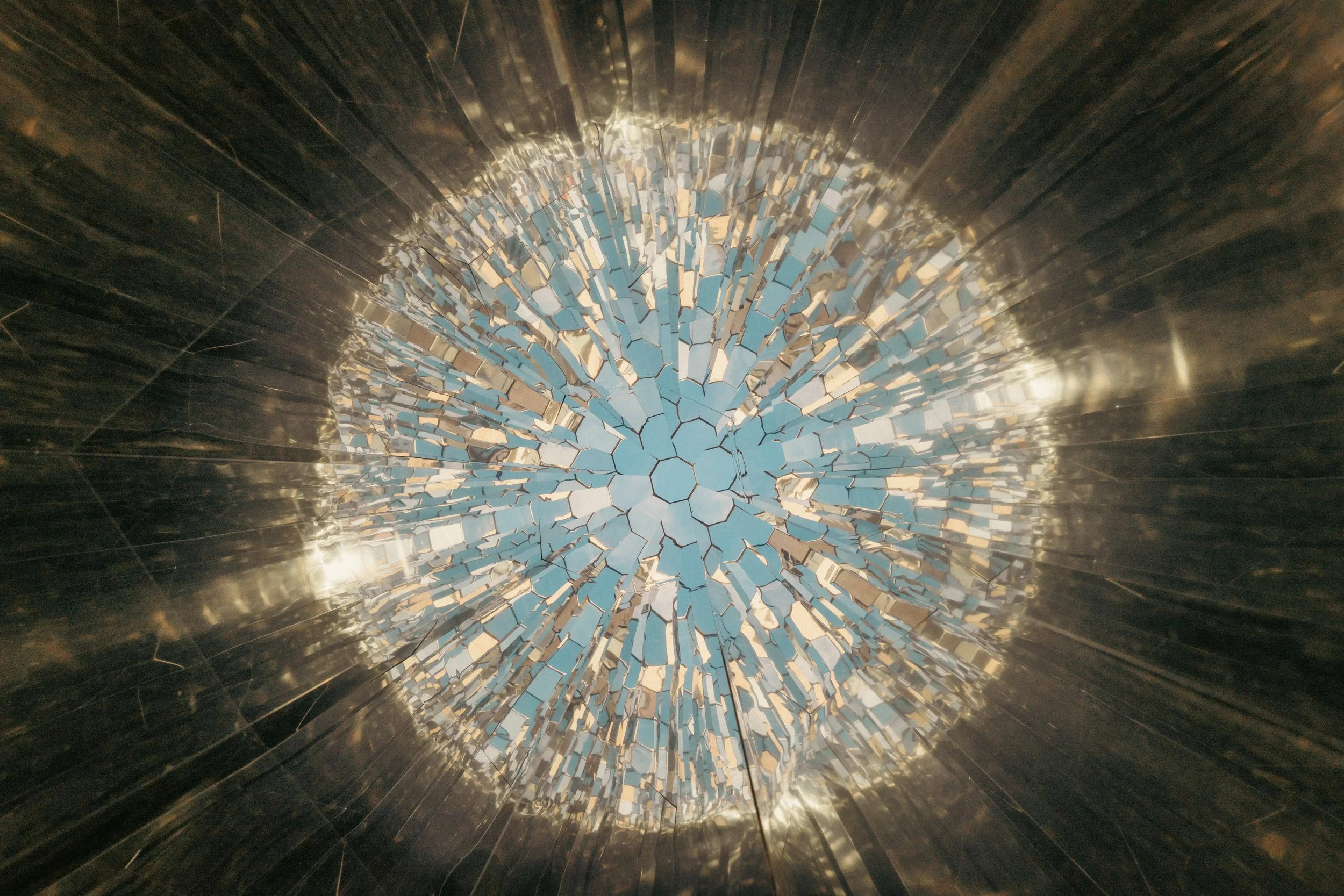 A circular mirror mosaic with cracked tiles, reflecting a cloudy sky.