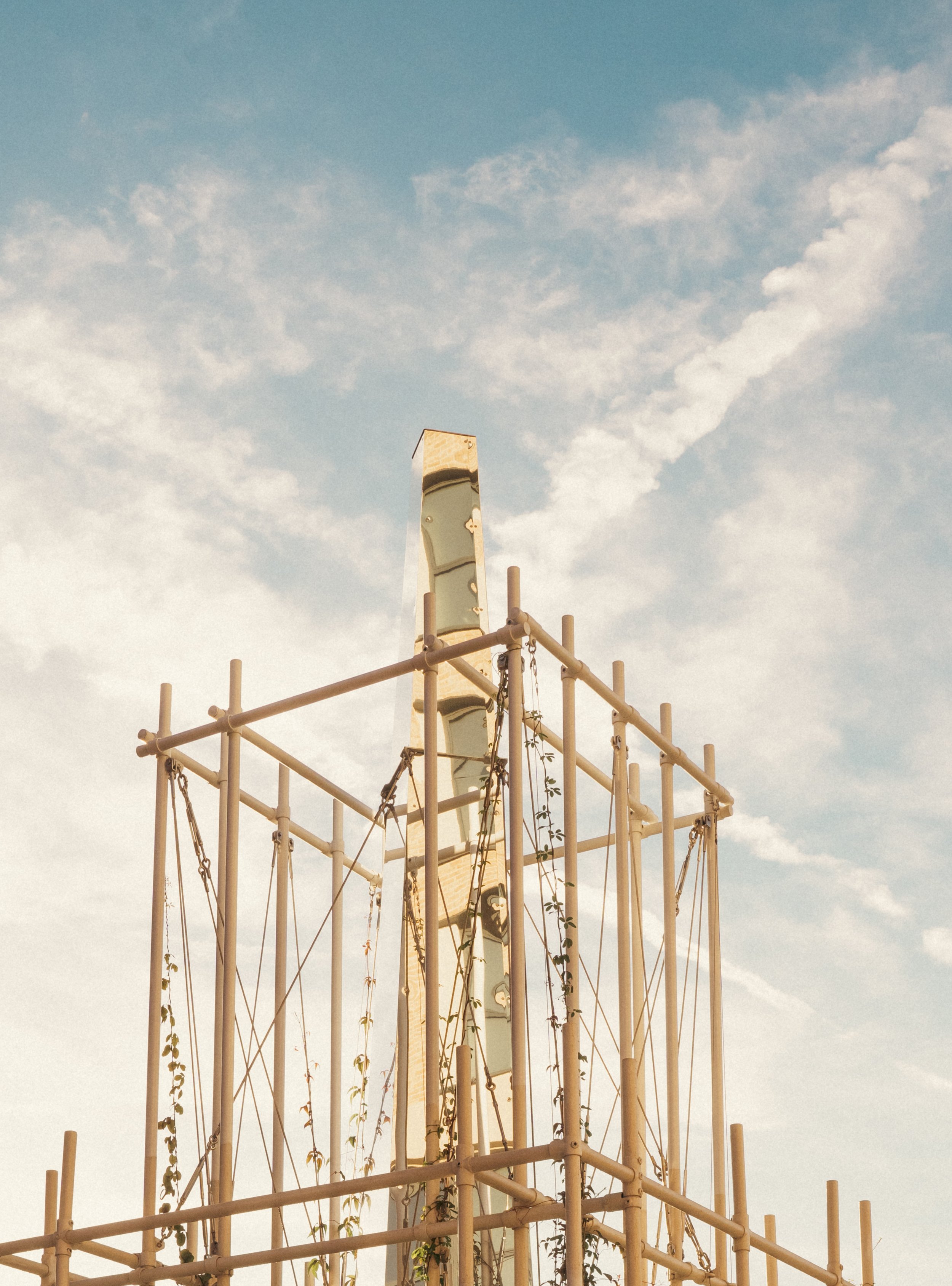 A playground structure with multiple swings and a tall slide, set against a bright blue sky with scattered clouds.