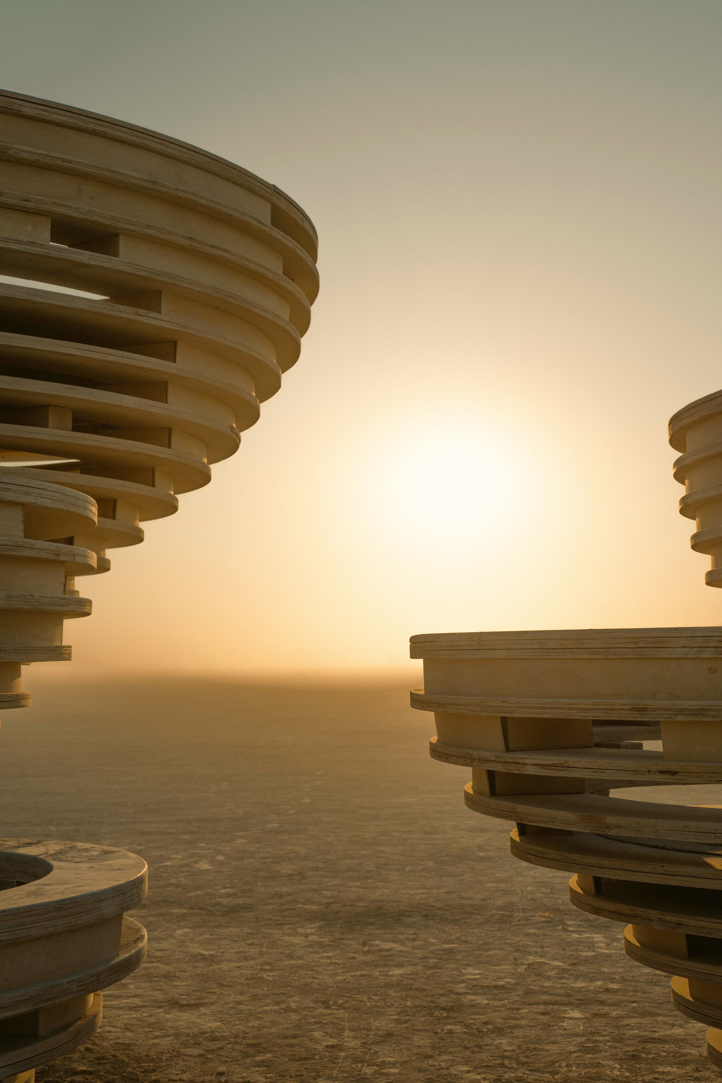 Stacked wooden chairs on a sandy beach at sunset.