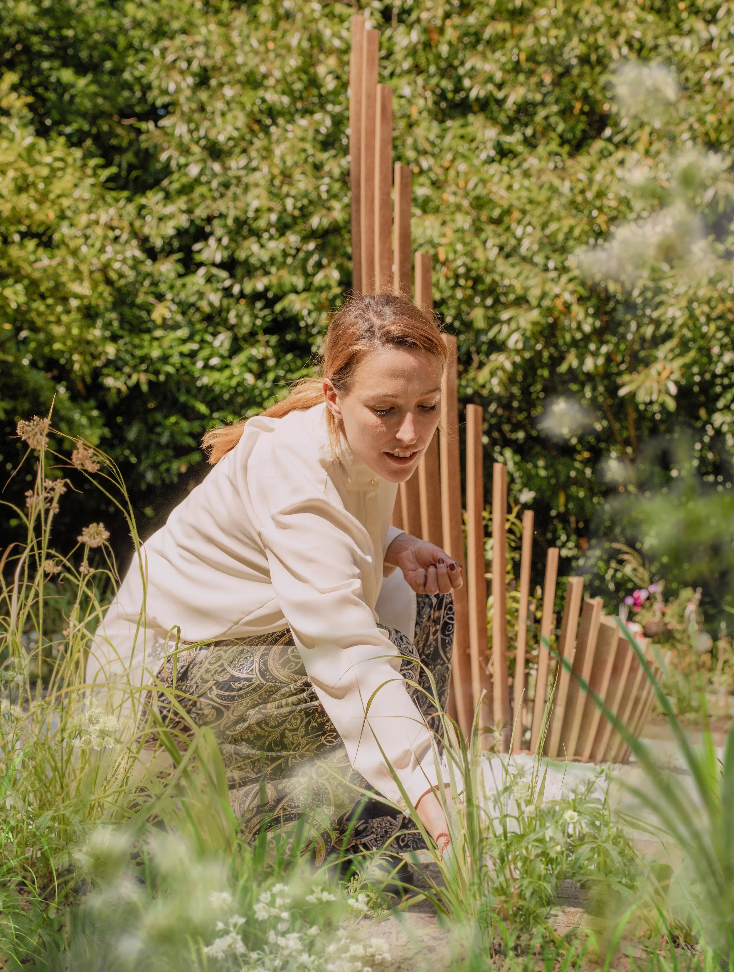 Woman planting or tending to plants in a garden surrounded by greenery and tall plants.