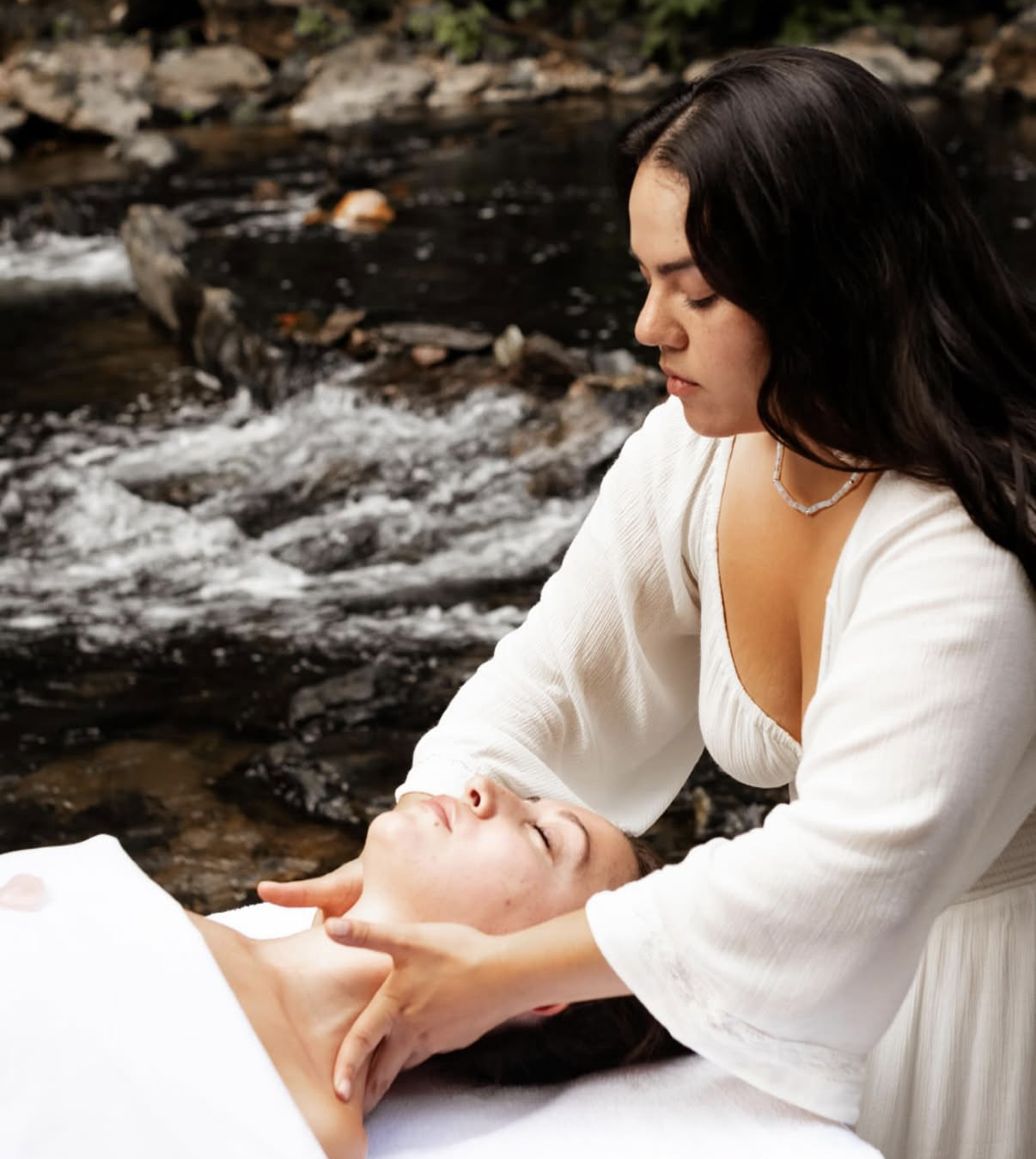 A woman receives a massage outdoors by a stream.