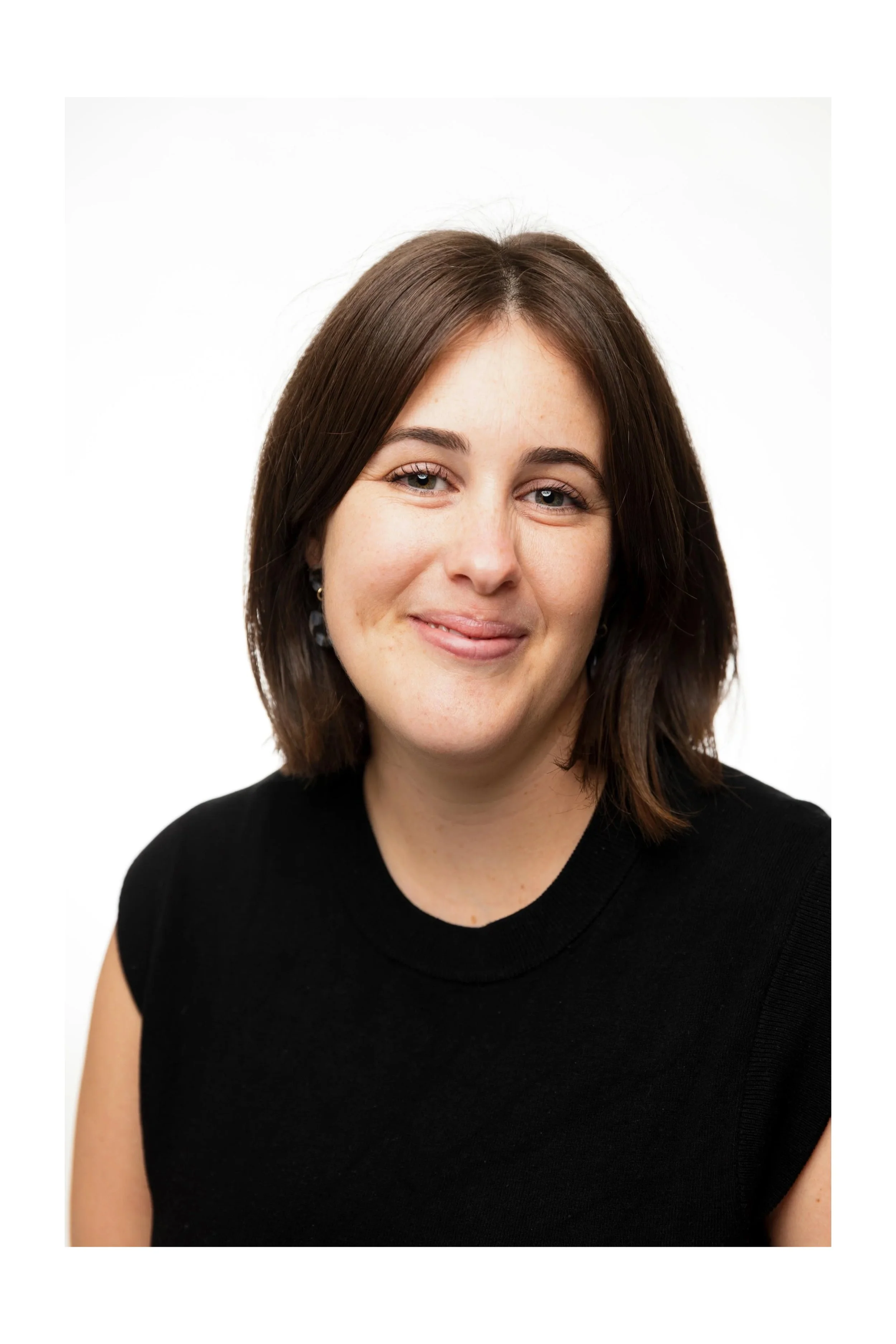 A woman with shoulder-length brown hair, smiling, wearing a black sleeveless top, against a white background.