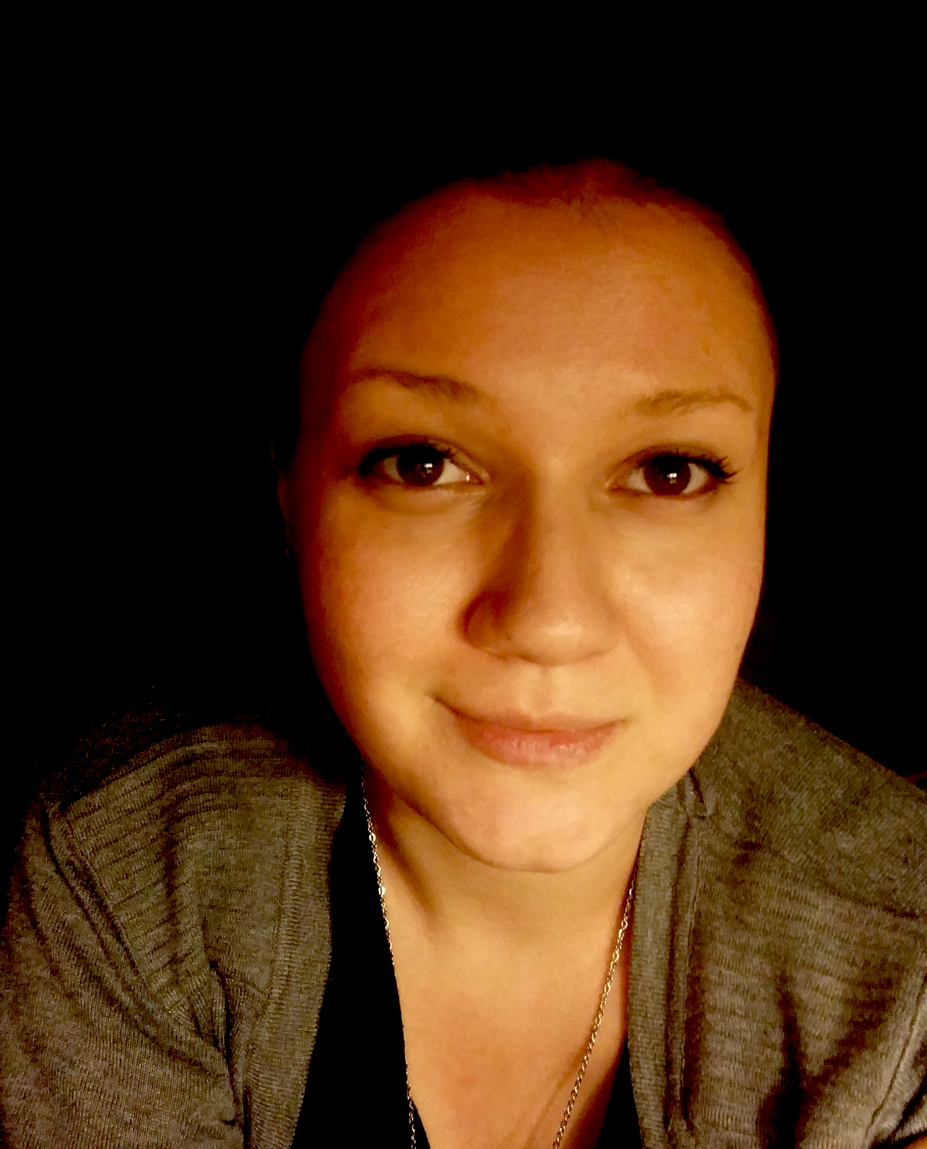Close-up of a woman, smiling slightly, wearing a gray sweater, against a dark background.