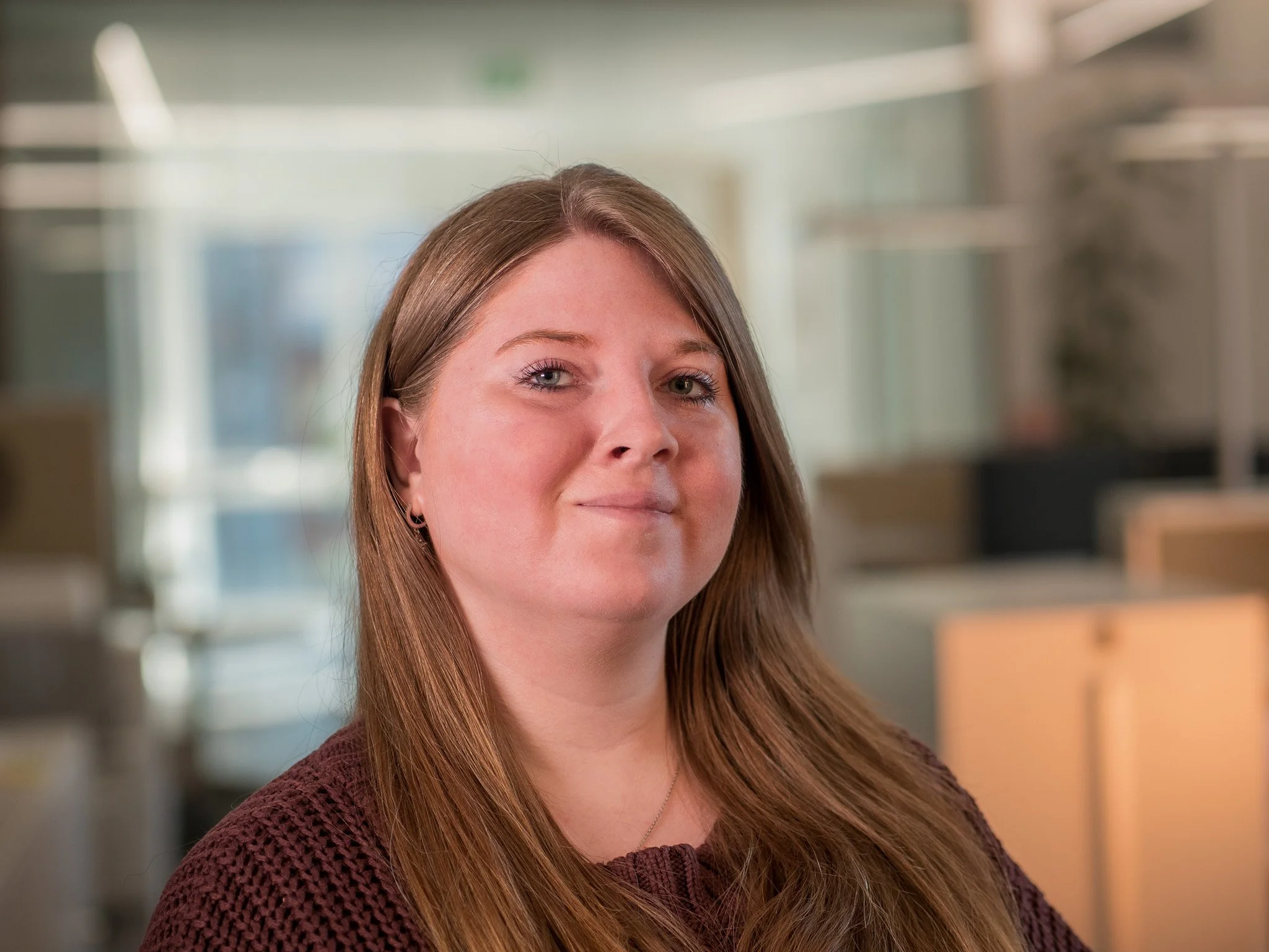 Ein Porträt einer jungen Frau mit langem braunem Haar in einem modernen Büro.