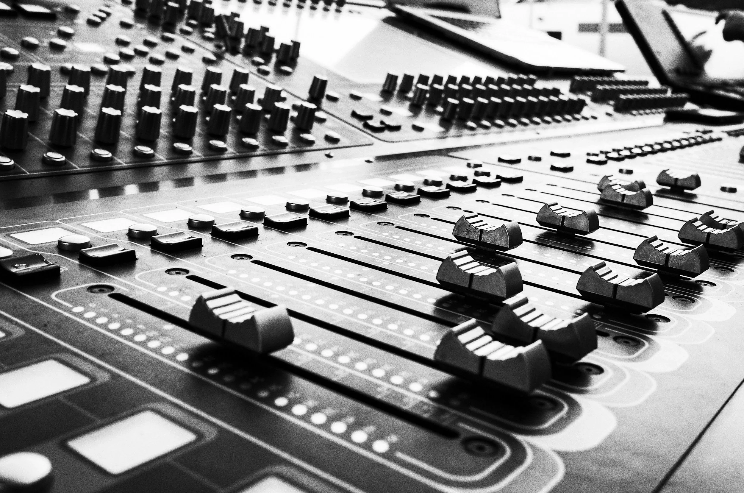 Close-up black and white photo of an audio mixing console with sliders, knobs, and buttons.