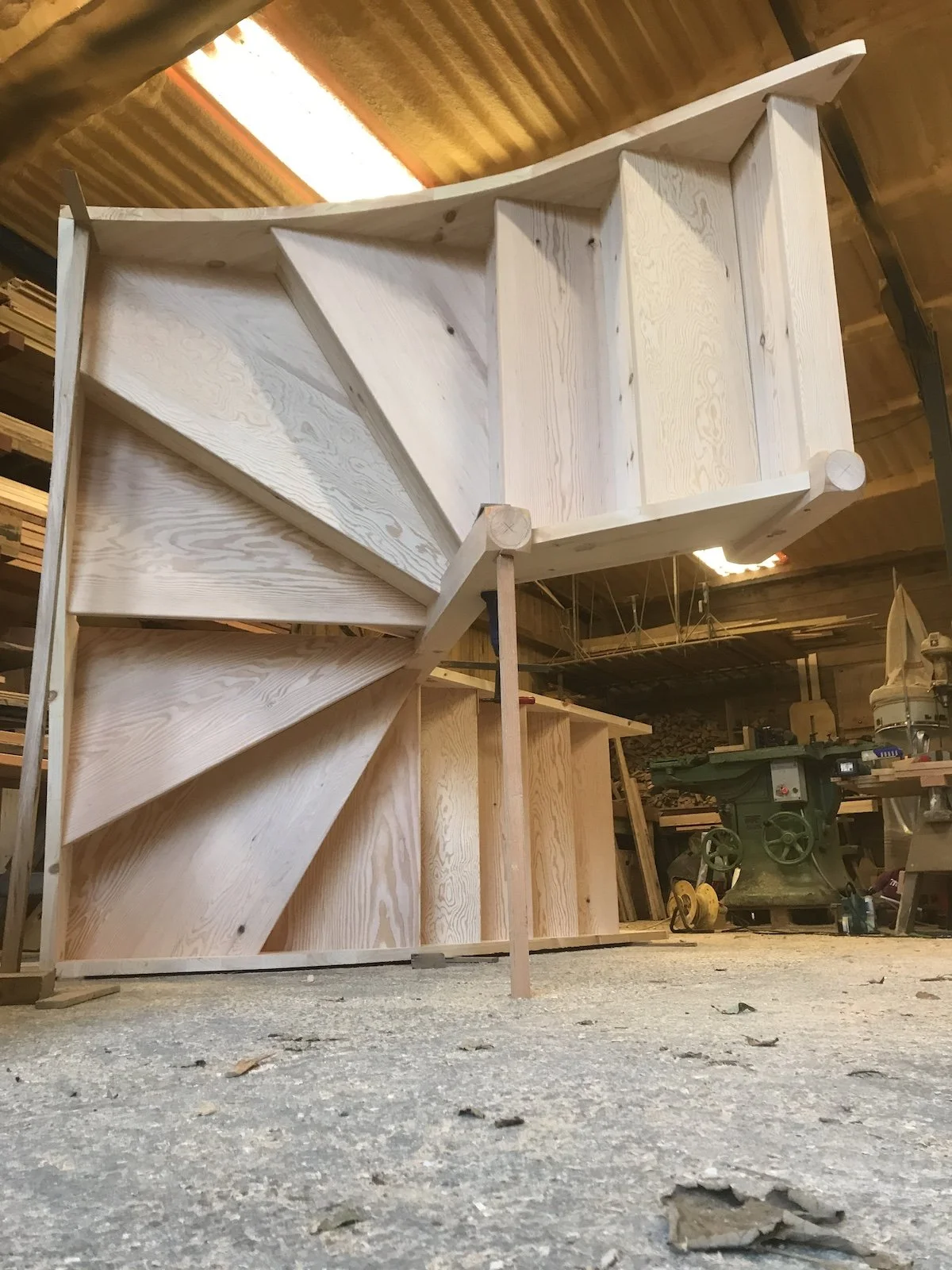 Interior of a woodworking shop with a large, partially assembled wooden staircase on the floor.