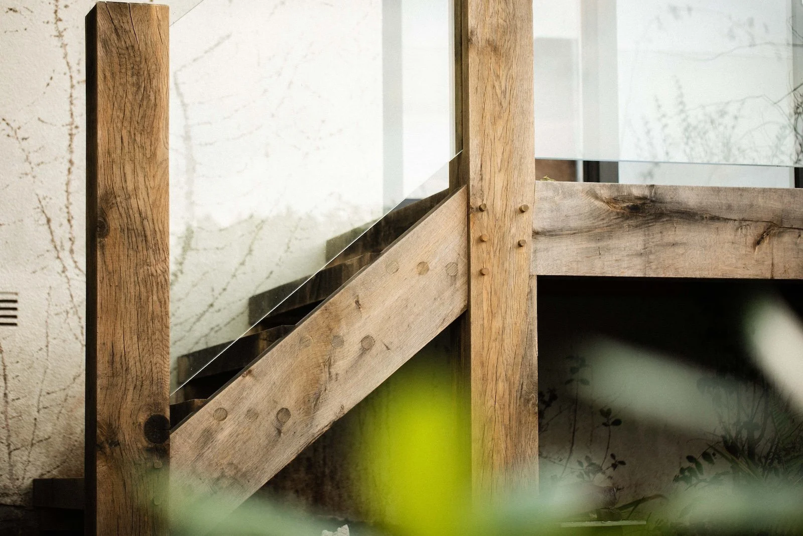 Close-up of a wooden staircase with glass railing and green plants in the foreground.