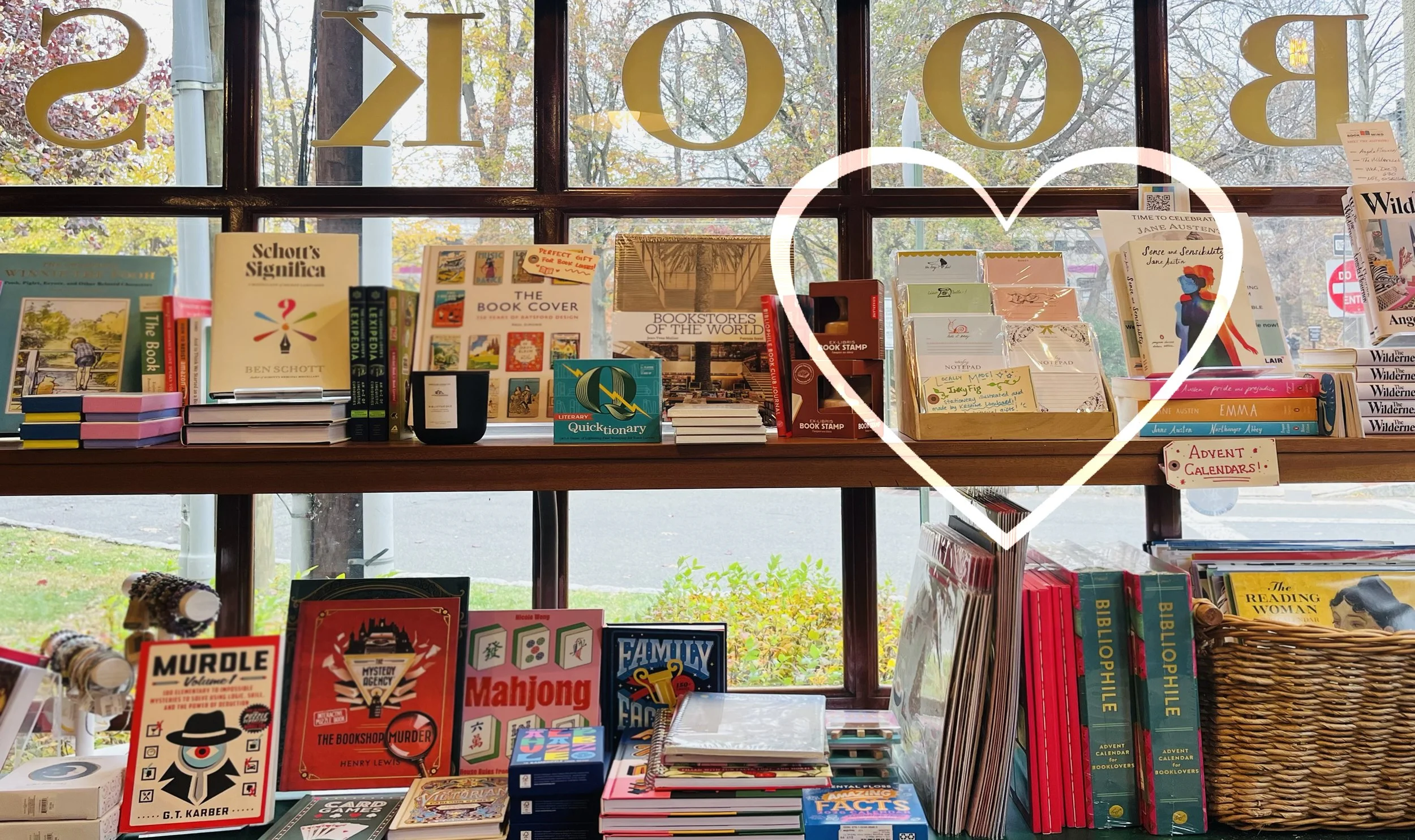 View of books and stationery inside a bookstore, with a large glass window in the background, outdoors with trees and street visible.