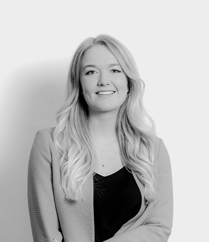 A black and white portrait of a young woman with long, wavy hair, smiling and wearing a blazer over a top.