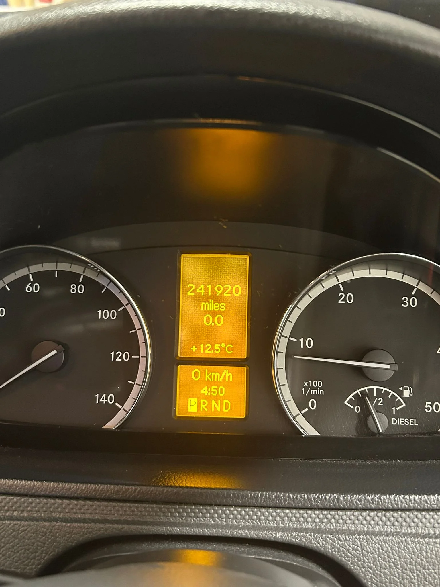 Car dashboard showing an odometer reading 241920 miles, temperature +12.5°C, a speed of 0 km/h, and the gear shift in park with 4:50 on the clock, fuel gauge nearly full, and tachometer at 0 RPM.