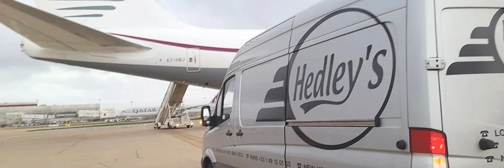 A Hedley's delivery van parked in front of a private jet at an airport.