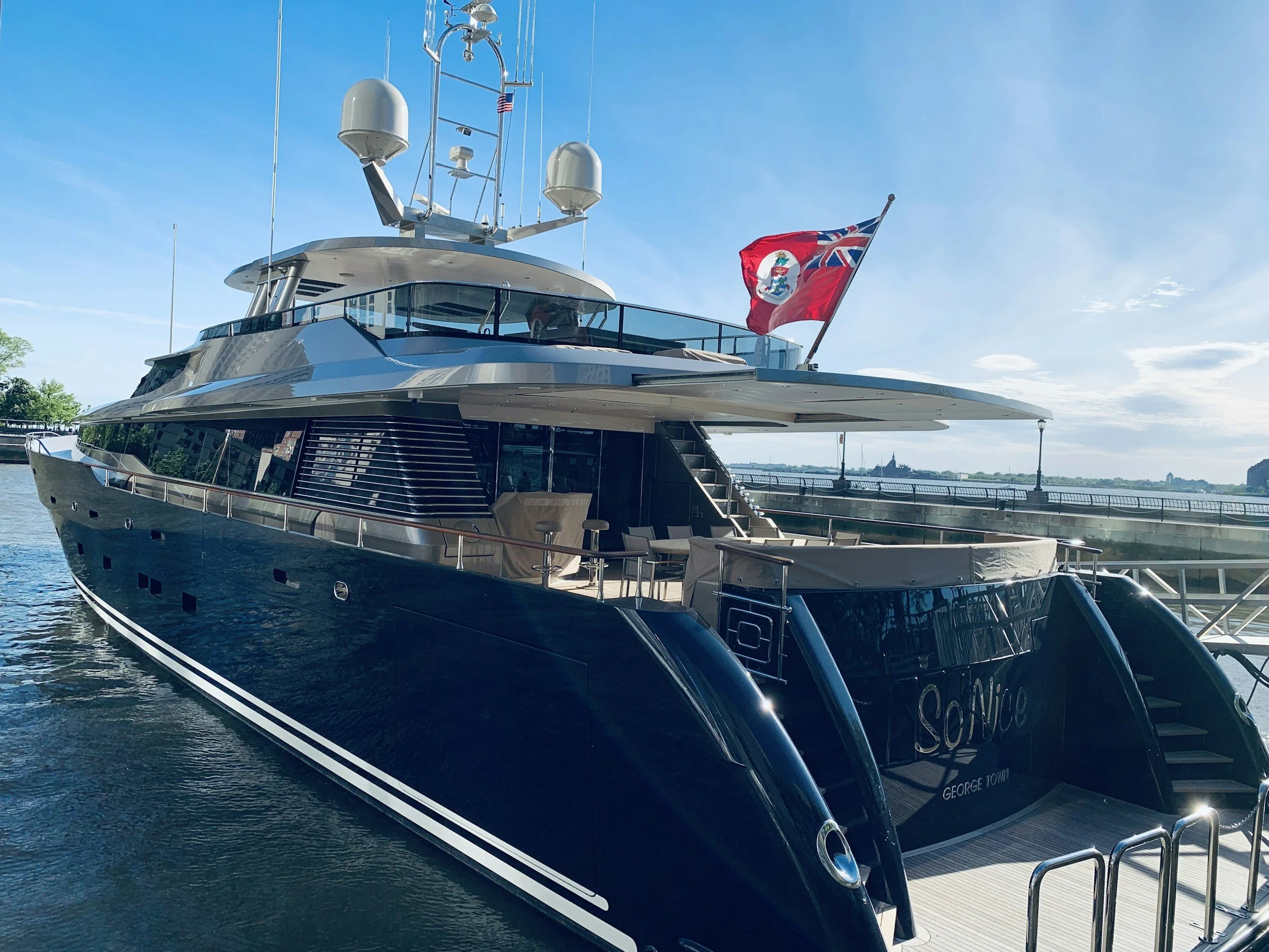 A luxurious black yacht docked at a pier on a sunny day, with American and flag of the British Virgin Islands flying on the stern.