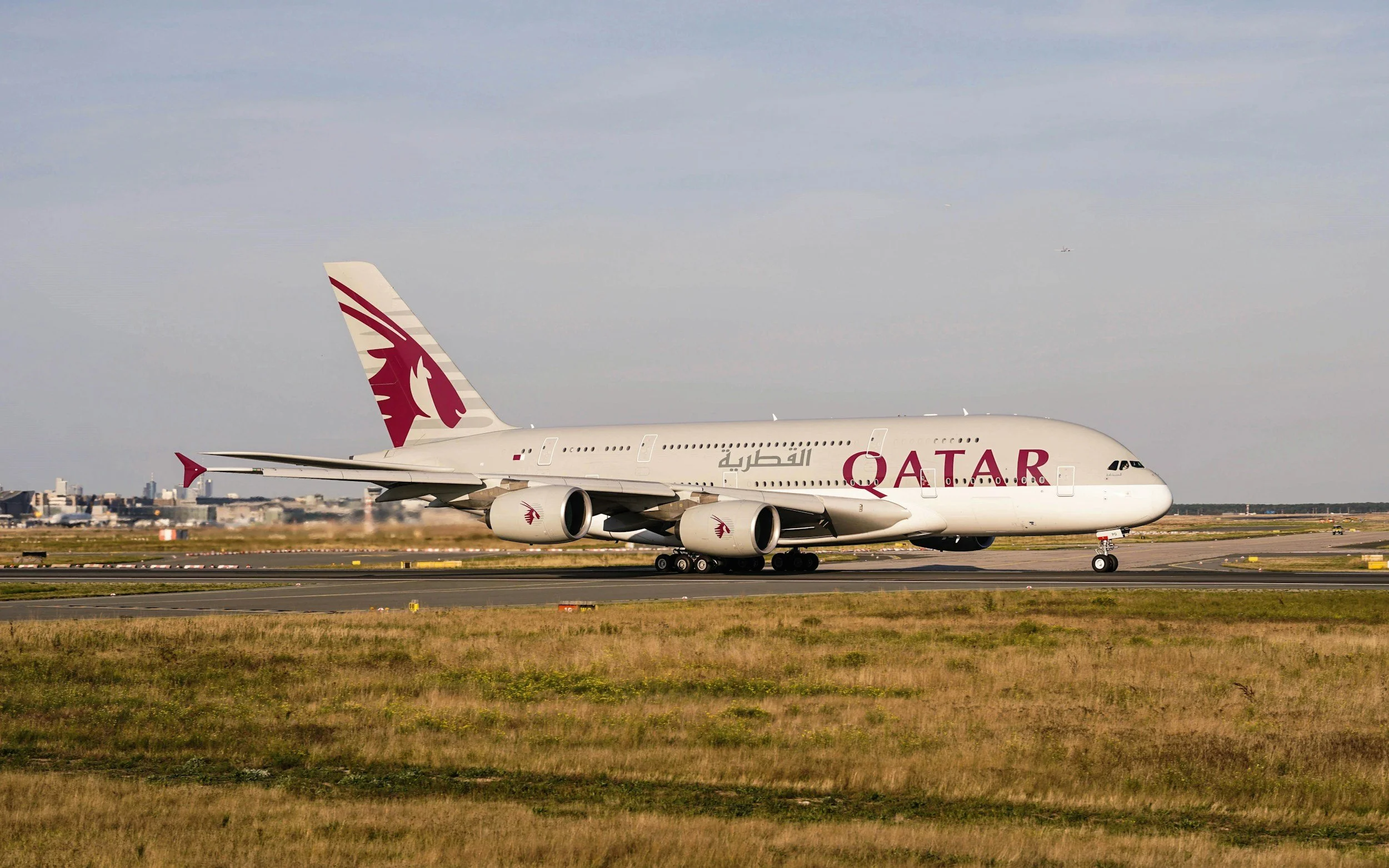 Qatar Airways airplane on runway at airport with city skyline in the background.