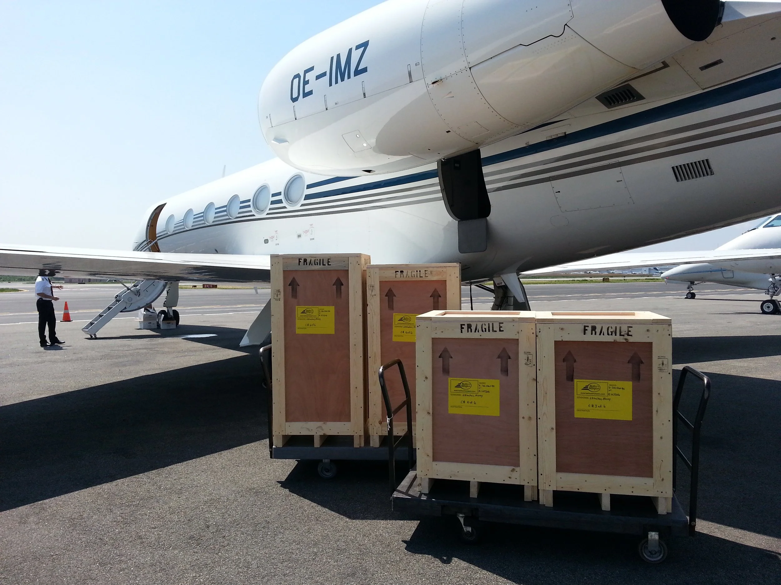 Large aircraft on tarmac with cargo crates labeled 'fragile' and a person nearby, under clear sky.