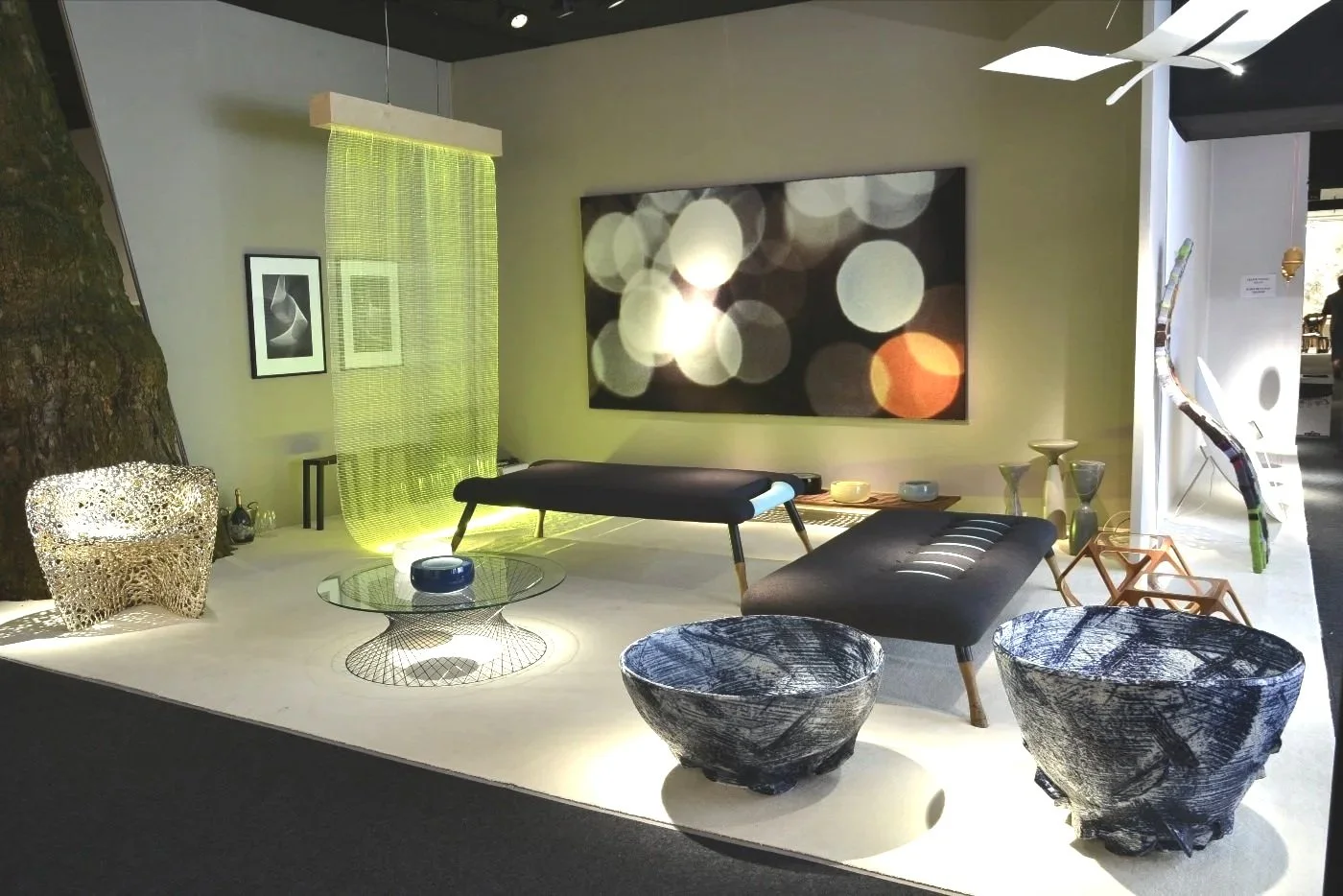 Modern living room with contemporary furniture including black and wooden loungers, artistic bowls, a large abstract artwork on the wall, decorative vases, and unique light fixtures, illuminated by soft lighting.