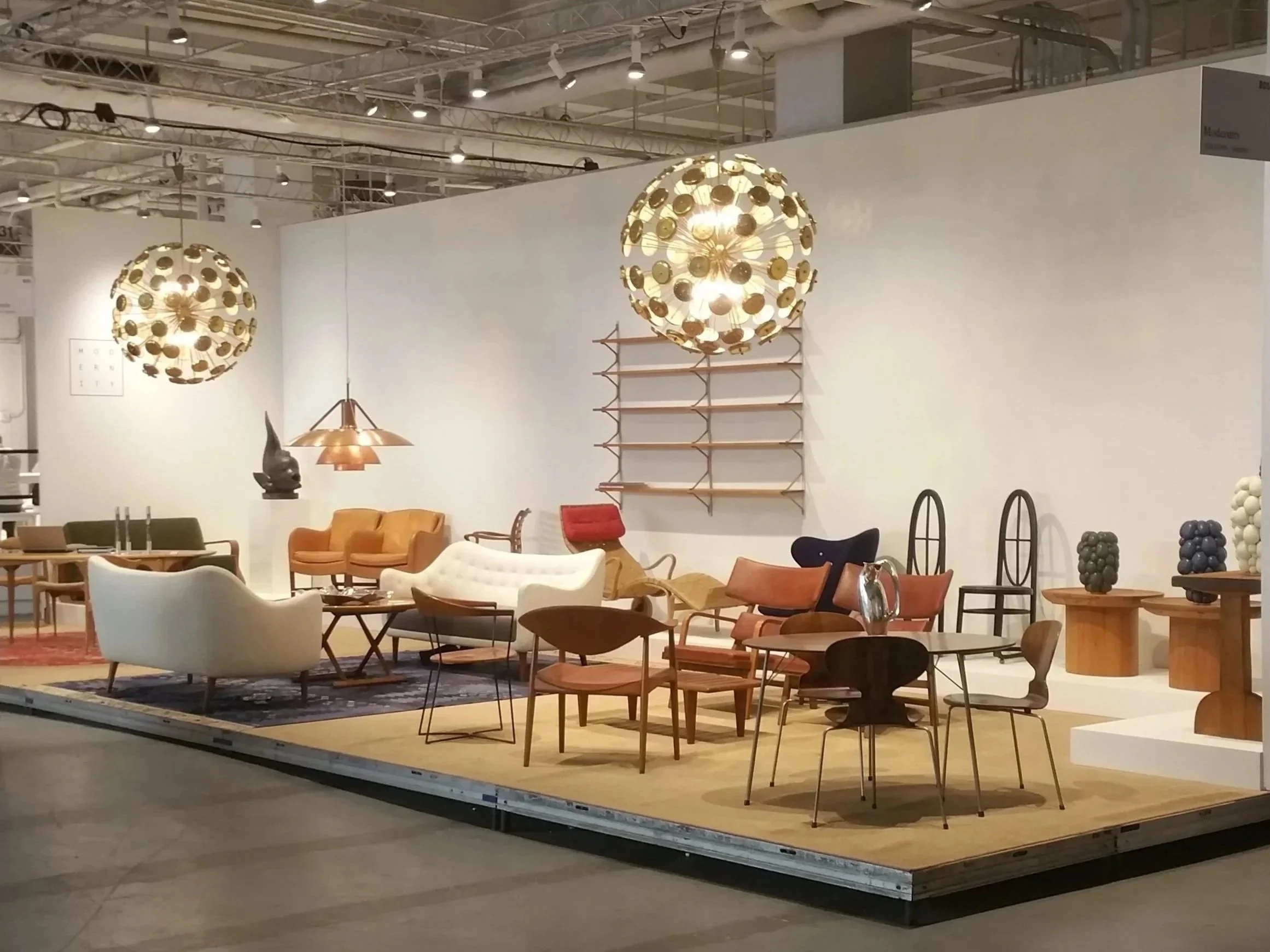 Display of modern furniture including sofas, chairs, tables, and lighting fixtures at a furniture exhibition.