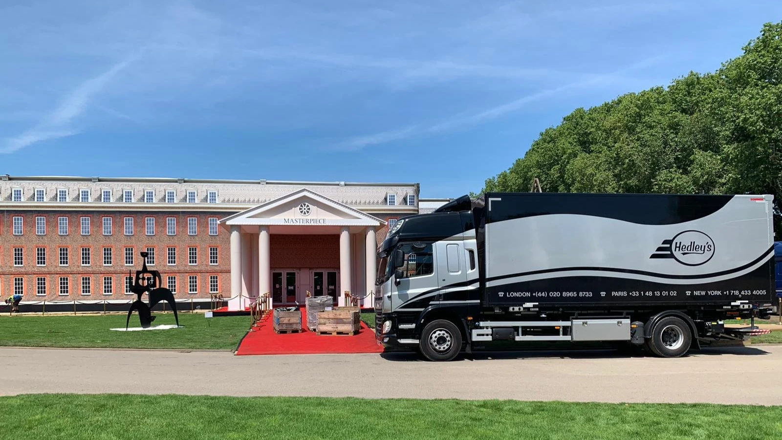 A classic Parisian-style building with tall windows and intricate architectural details, behind a black and white delivery van with Hedley's branding parked on a cobblestone courtyard.