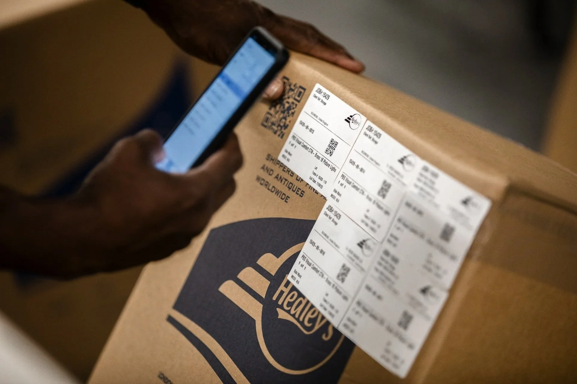 A person is scanning a barcode on a brown box with a smartphone.