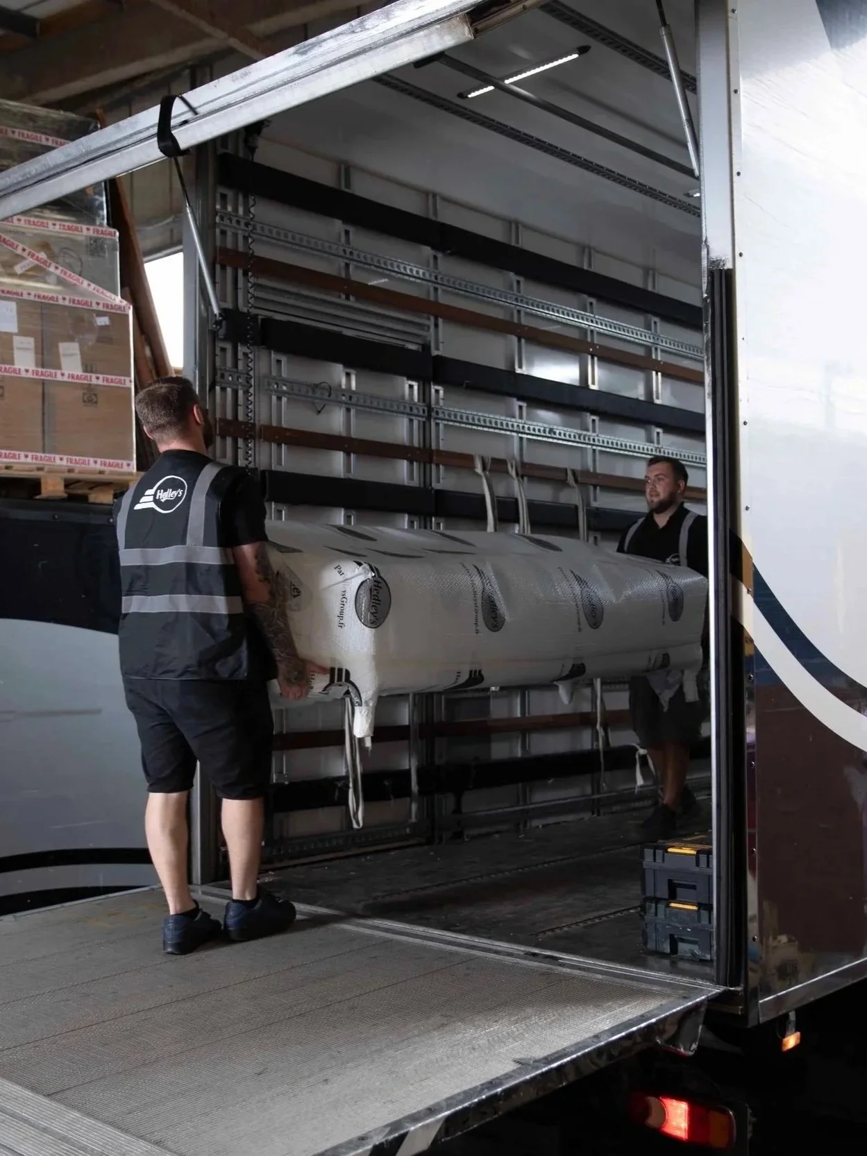 Two men loading a large wrapped item into the back of a truck with an open side door.
