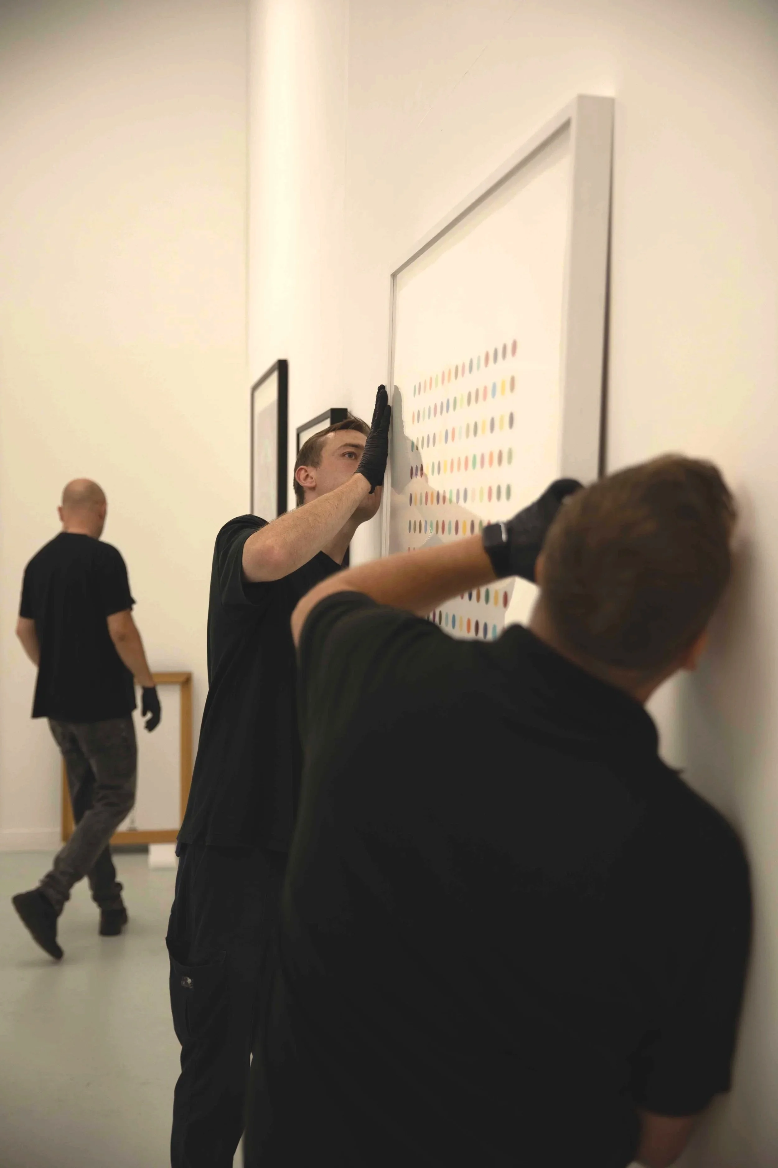People examining artwork with colorful patterns on a white wall in an art gallery.