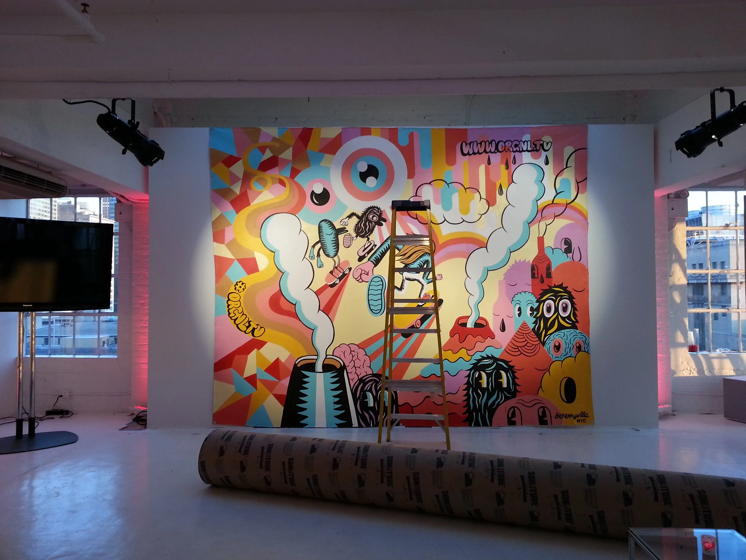 Colorful graffiti mural on a wall in an art gallery with a ladder in front of it, featuring cartoonish characters, abstract shapes, and smoke/cloud patterns.