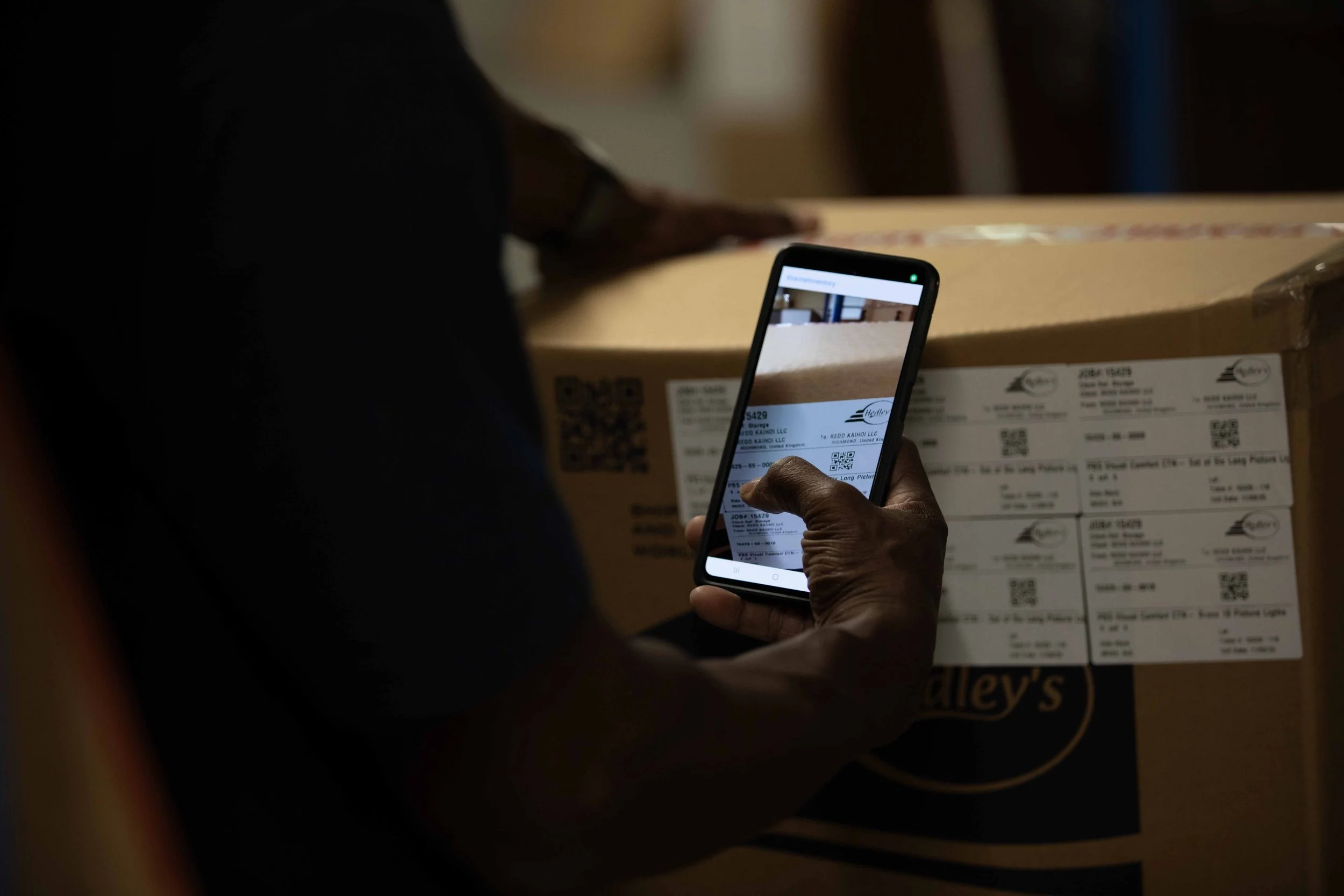 A person holding a smartphone capturing the barcode and shipping label on a cardboard box.