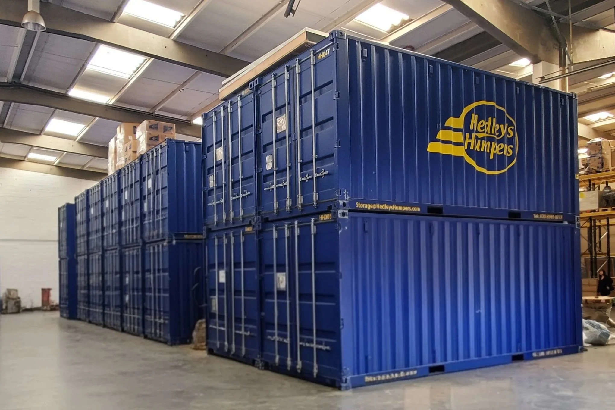 Large blue shipping containers stacked inside a warehouse, with the logo 'Hedley's Humpers' on the side.