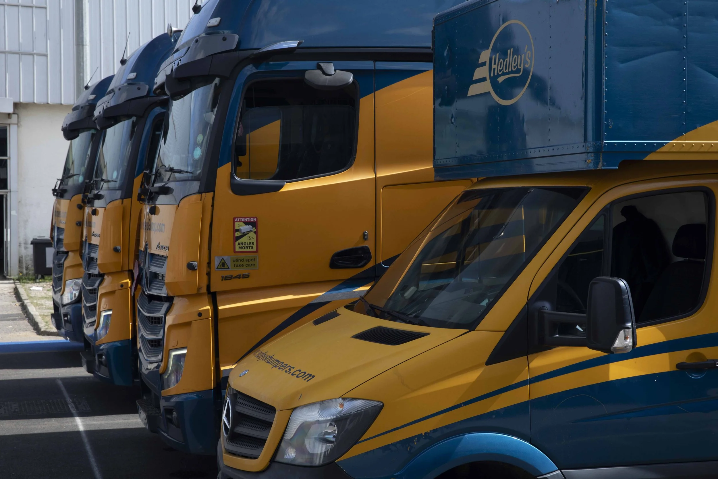 A row of yellow and blue delivery trucks parked outside a building.