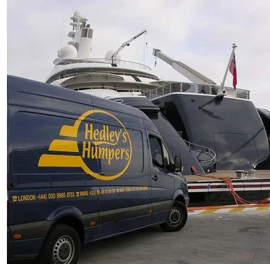 Yacht docked at a marina with a Hedley's Humpers delivery van parked nearby.