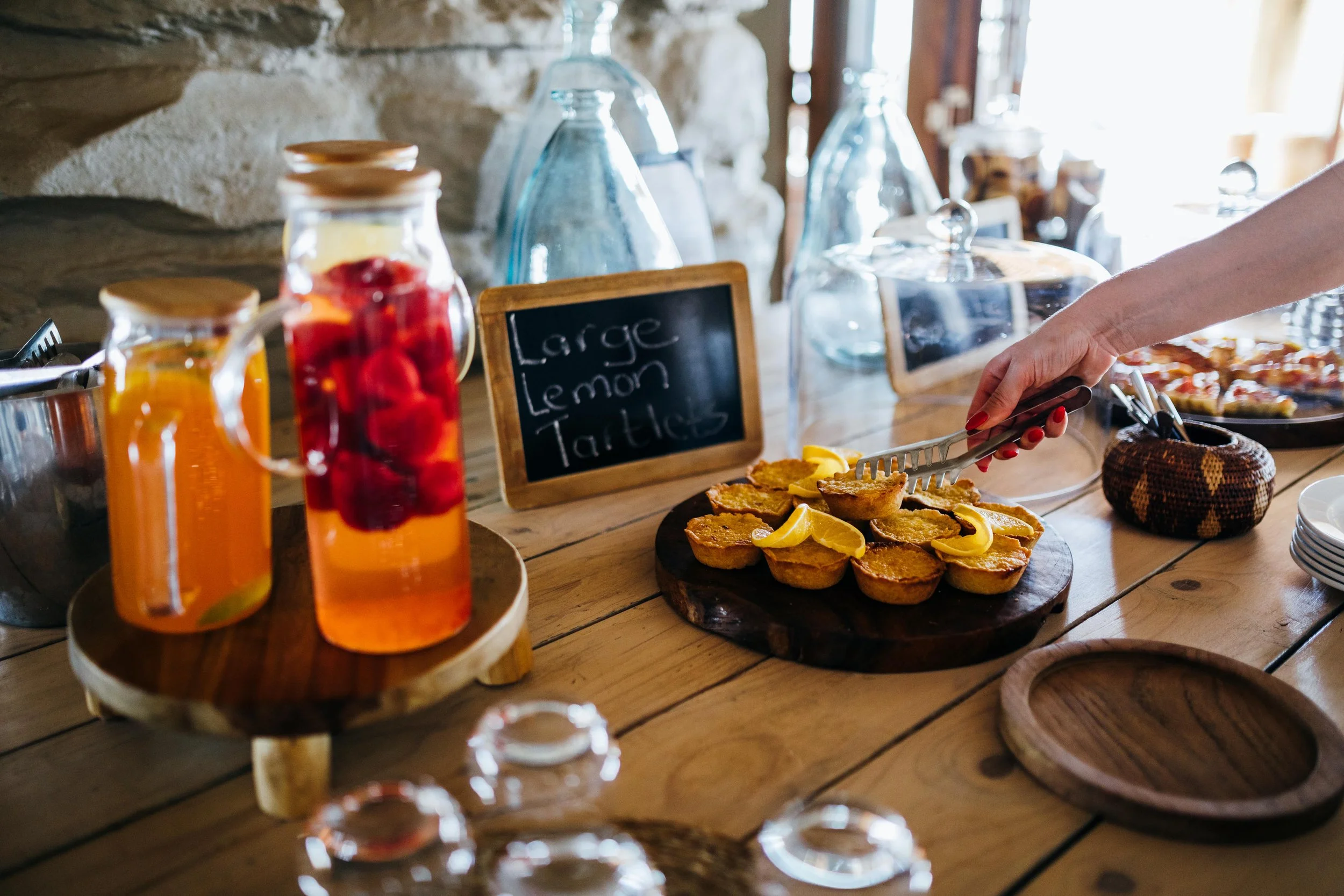 Breakfast buffet featuring lemon tarts, fruit-infused waters, and a small chalkboard sign that reads 'Large Lemon Tarts.'