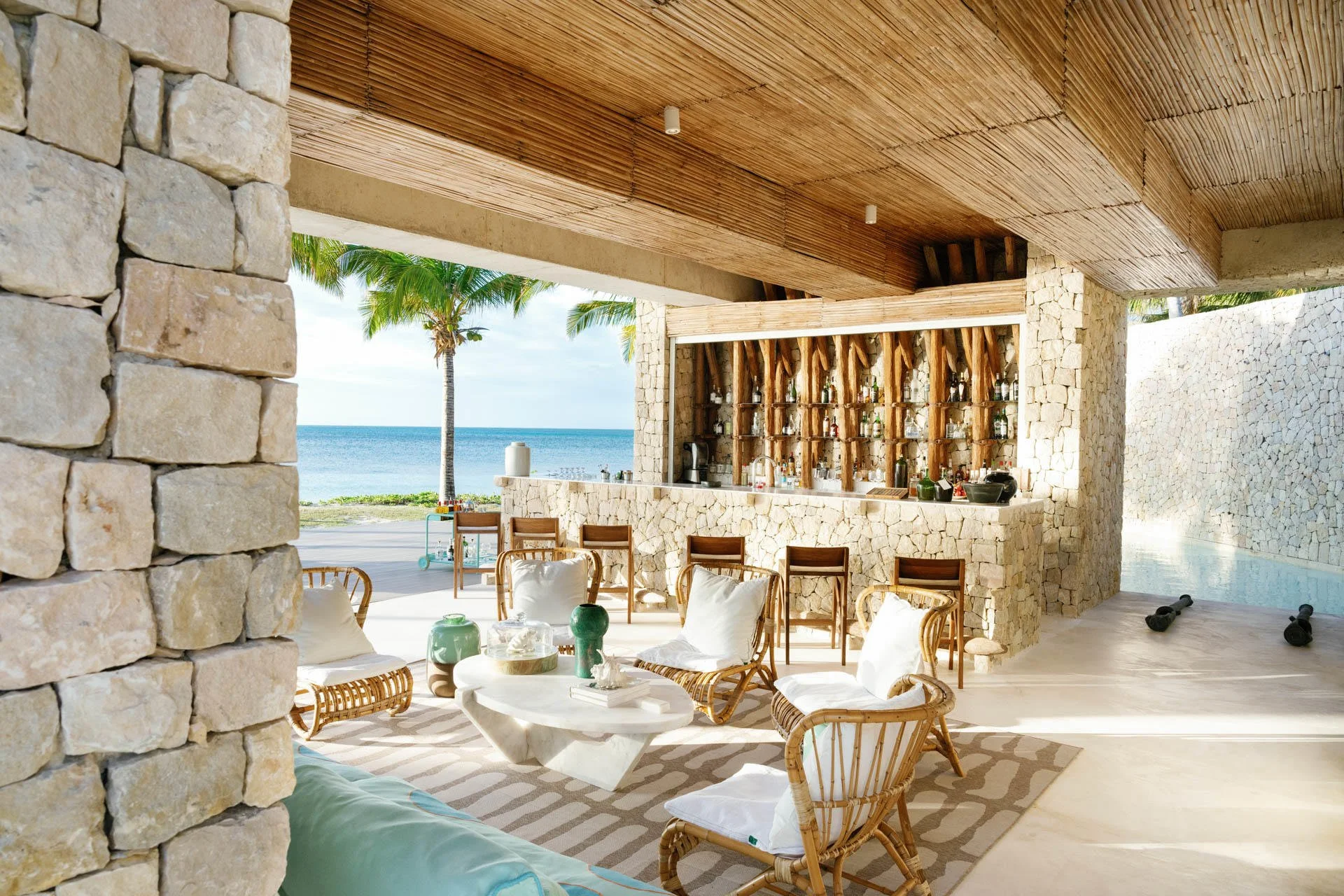 Beachside bar with wicker chairs and bar counter, overlooking the ocean with palm trees in the background