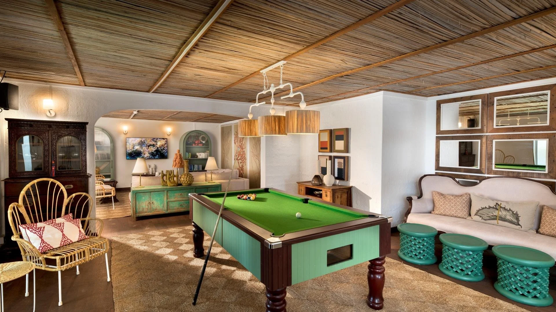 Living room with a pool table, a beige sofa, chairs, a television, and decorative items, featuring wooden ceiling and vintage-style furniture.