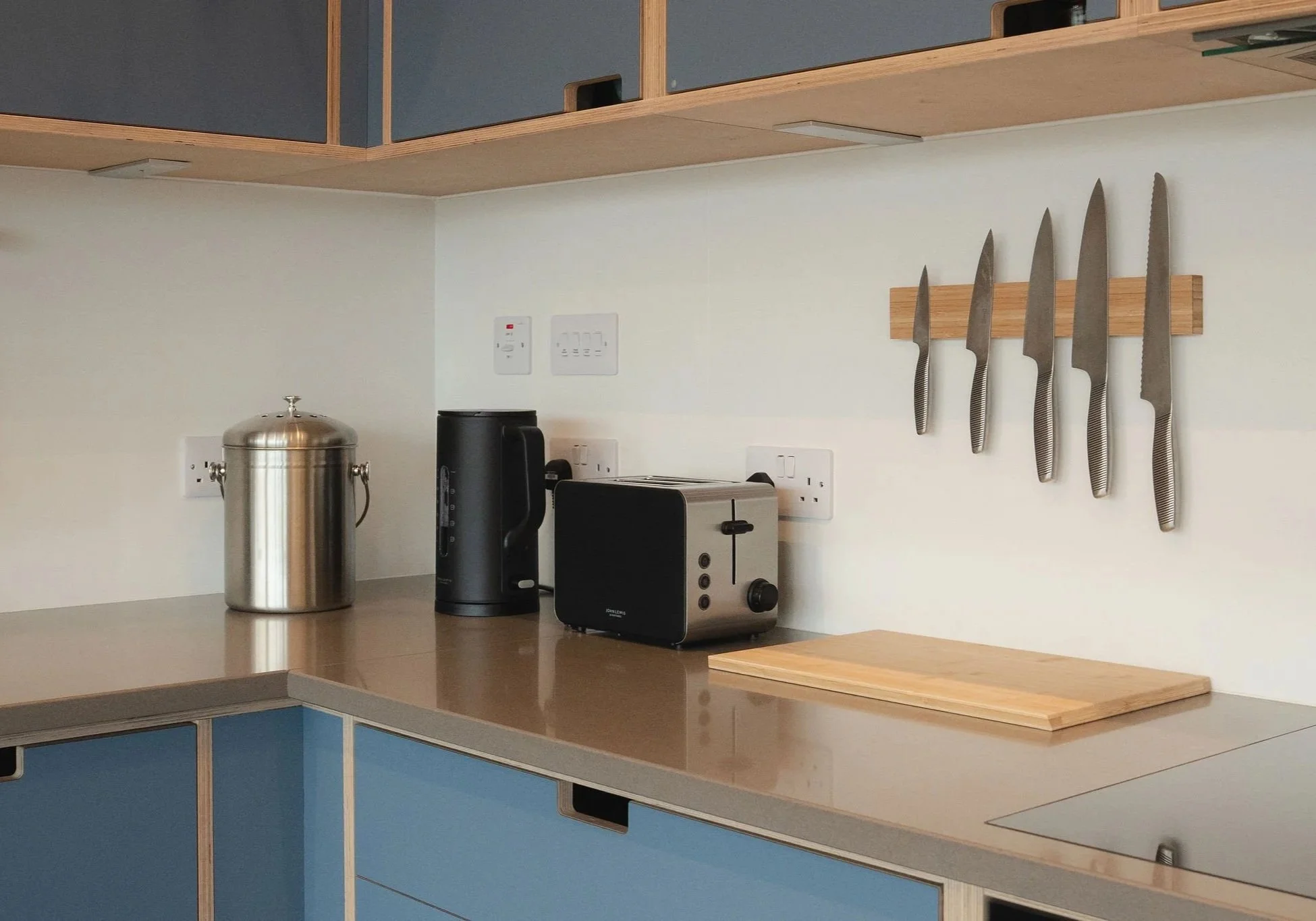 Küchenzeile mit blauen Schränken, einem Edelstahlbehälter, einer Kaffeemaschine, einem Toaster und einem Messerhalter aus Holz für sechs Messer.