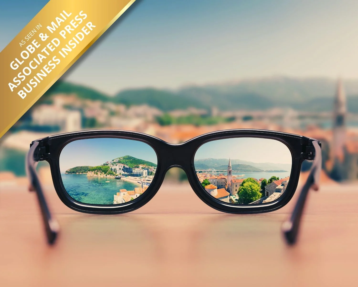 Sunglasses resting on a surface, reflecting a coastal cityscape with buildings, a hill, and water, with a blurred background of the same cityscape.