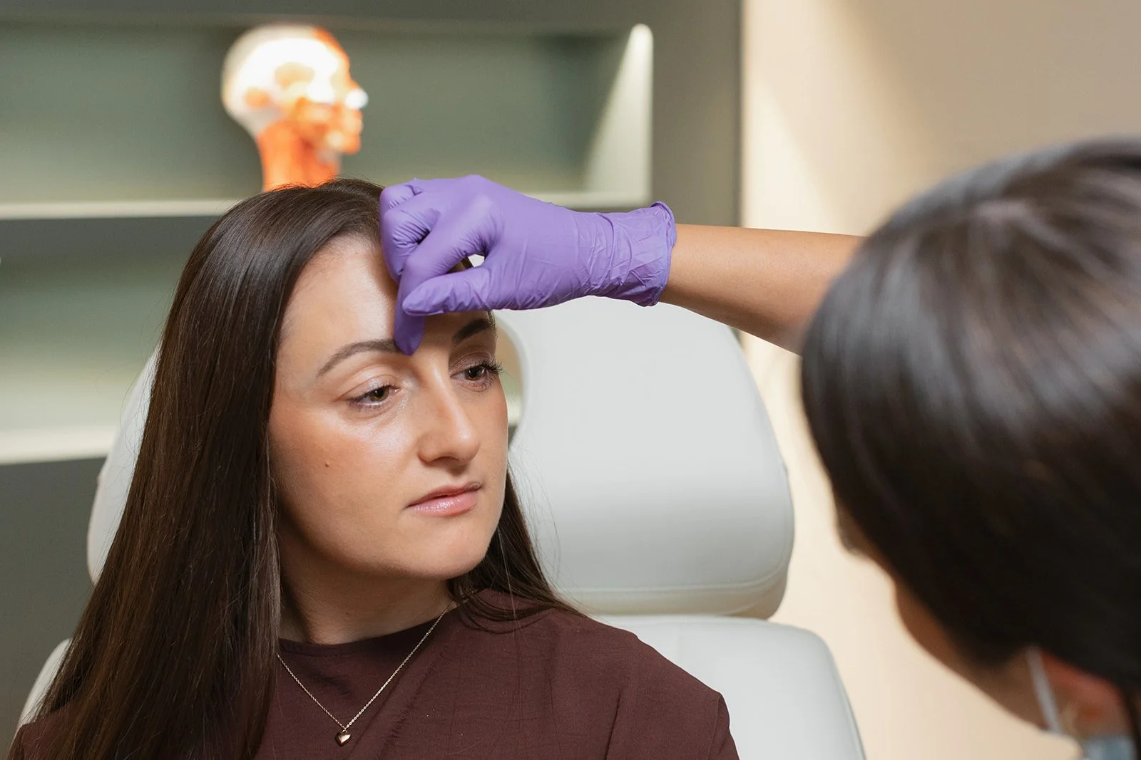 Clinician is wearing sterile gloves as she touches the face of a client, explaining how and where the treatment will be applied