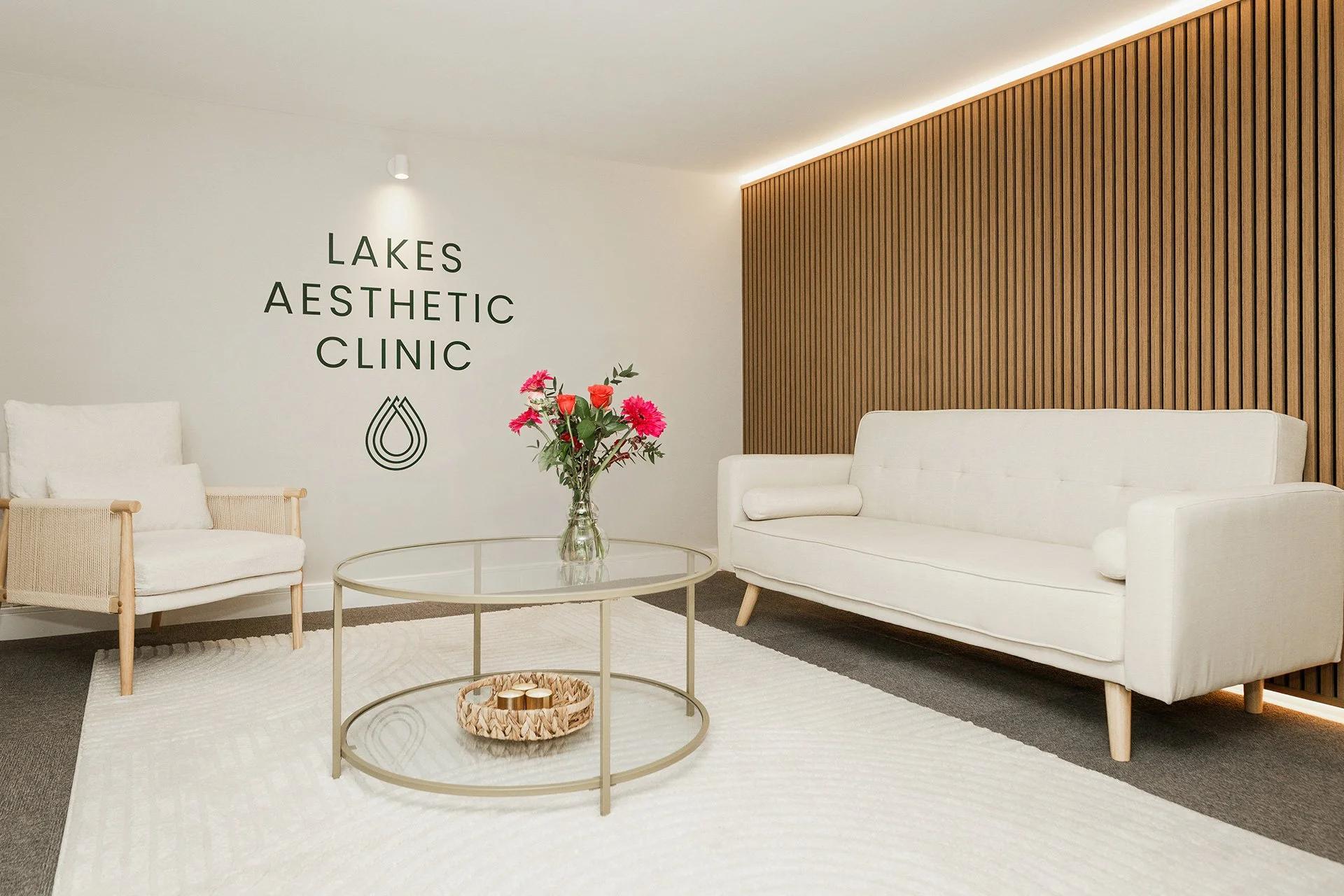 View of the Lakes Aesthetic Clinic lounge, a welcoming space with comfortable seating, mood lighting and nice flowers on the glass table