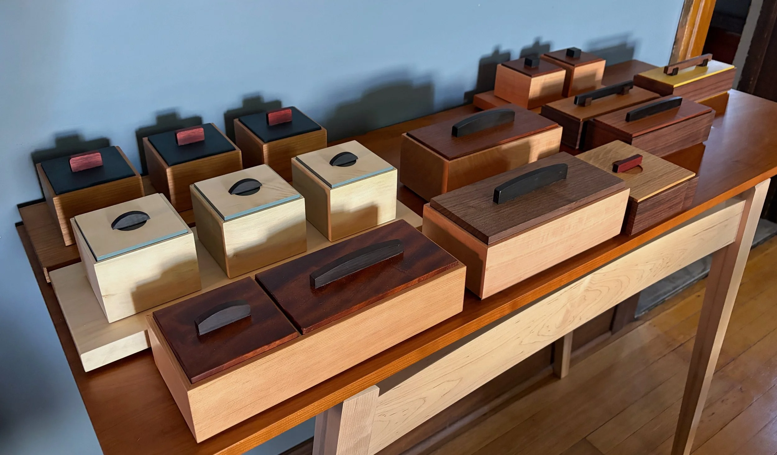A collection of wooden boxes with black handles and colored accents on a wooden table.