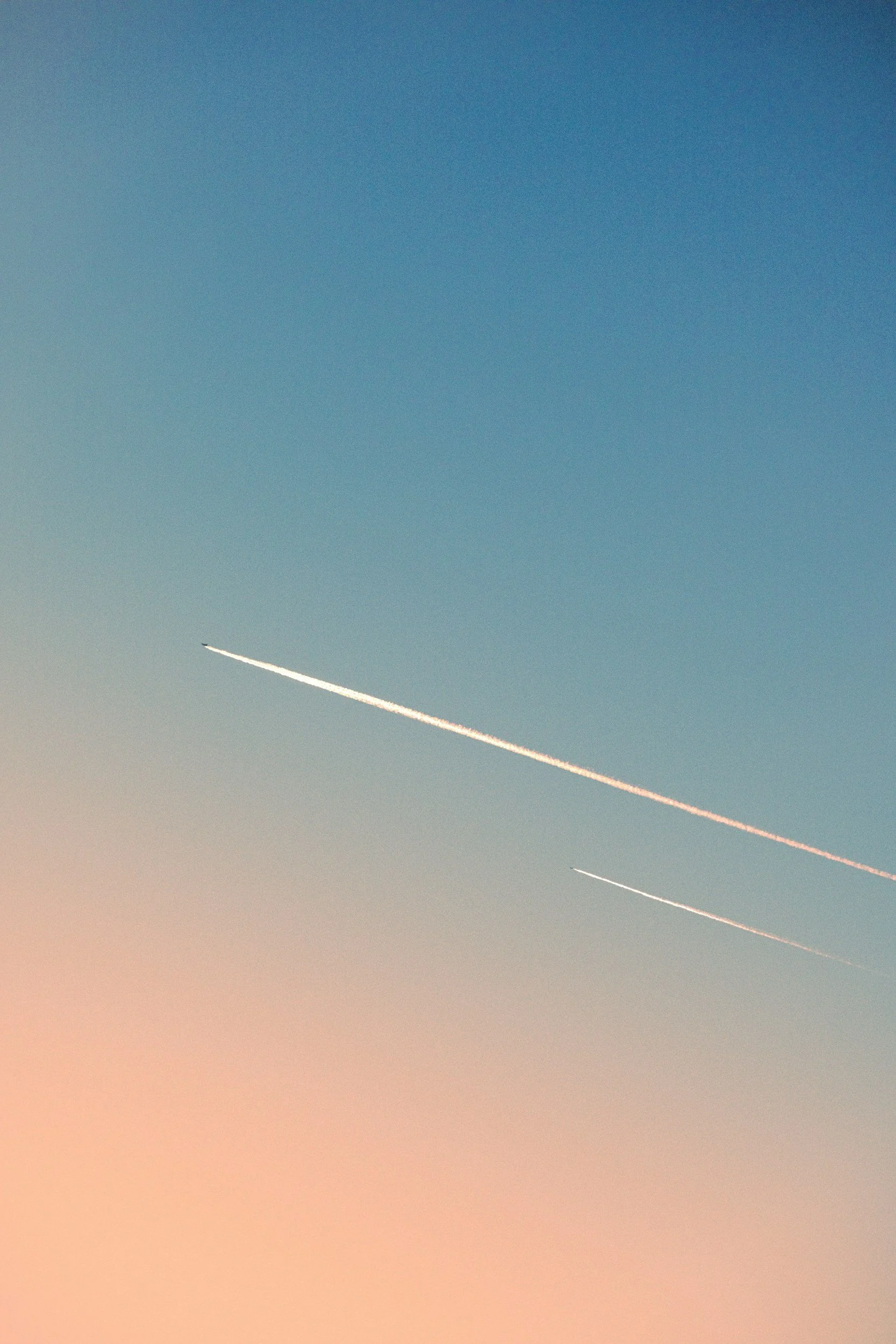 Two airplanes flying in the sky leaving contrails behind them during sunset or sunrise.