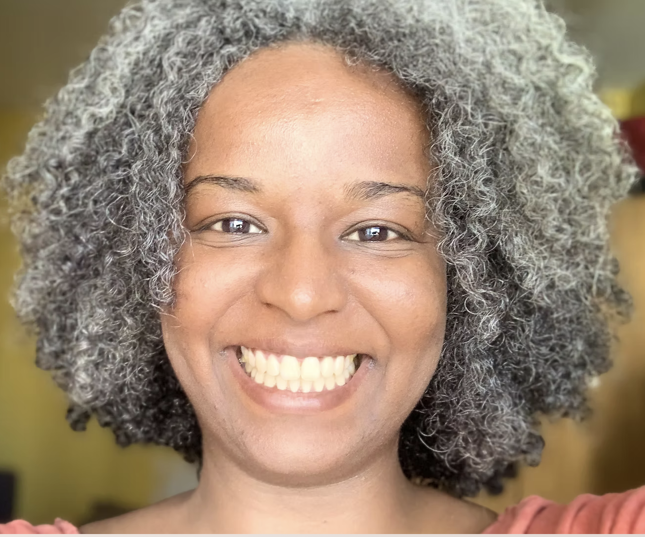 A woman with curly gray and black hair smiling directly at the camera.