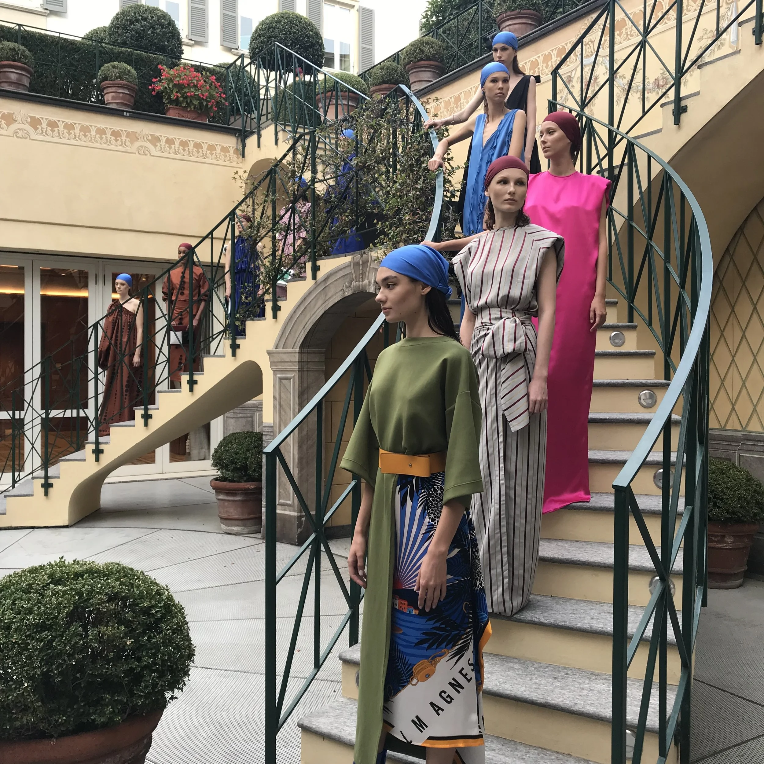 Several mannequins dressed in colorful clothing, including dresses and headscarves, standing on a staircase outdoors.