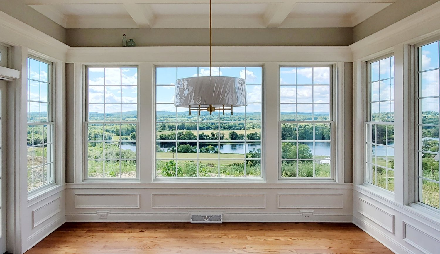 Sunroom with paneled walls and a coffered ceiling, windows on three sides overlooking the water