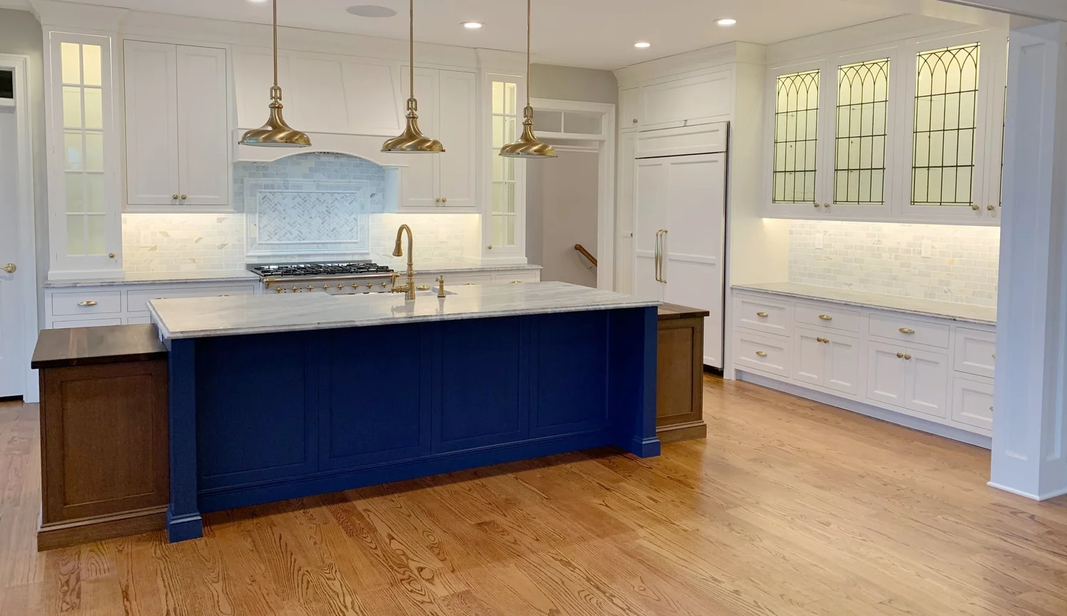 Kitchen with a navy island, brass pendants and leaded-glass cabinets