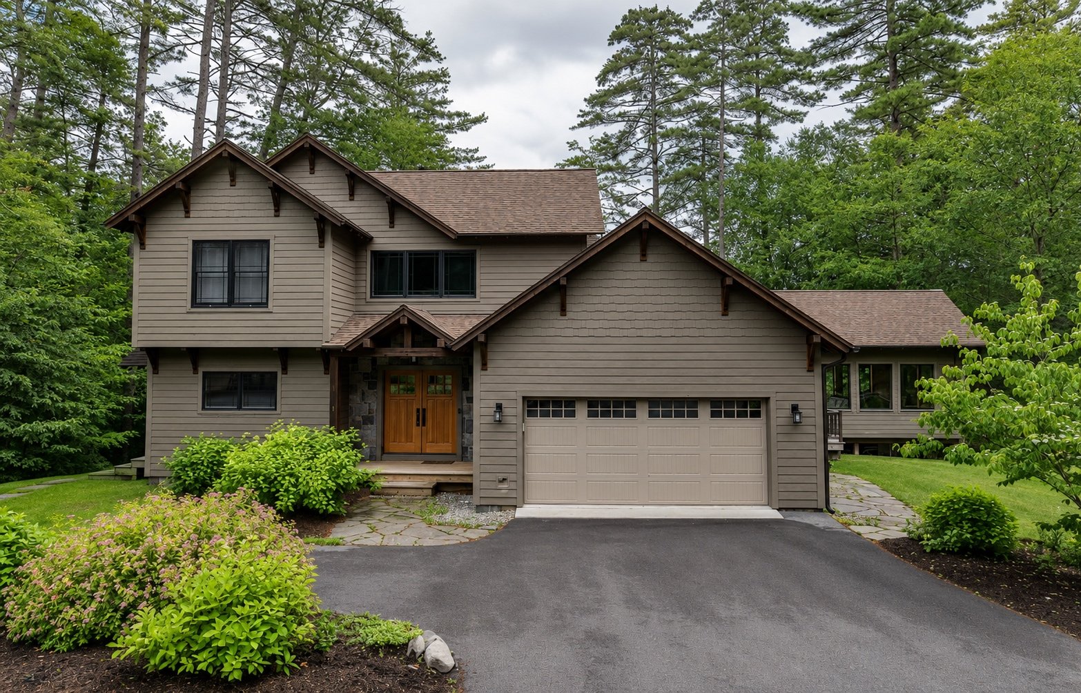 A modern two-story house with a brown front door, a two-car garage, surrounded by green trees, shrubs, and a driveway in a lush yard.